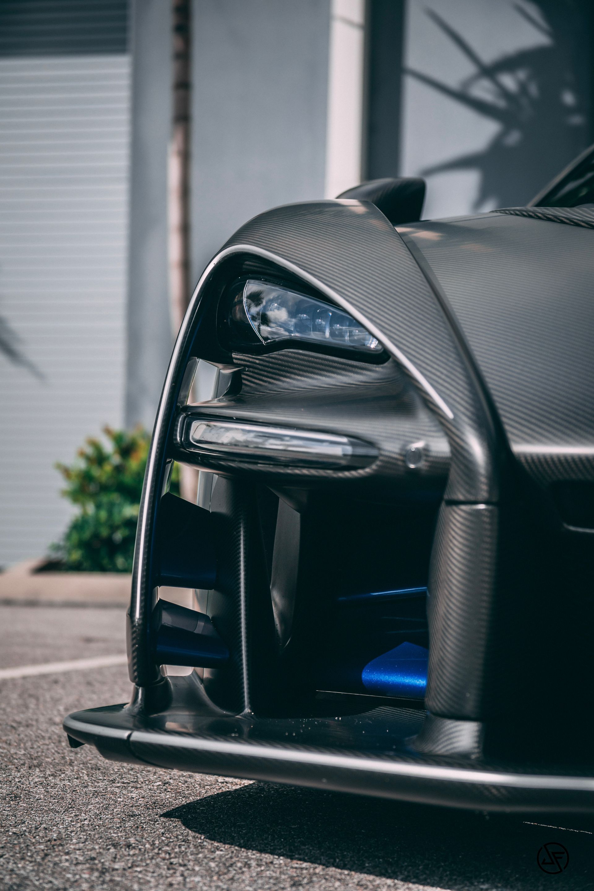 Close-up of a dark grey McLaren Senna's front end, with carbon fiber detailing and blue accents.