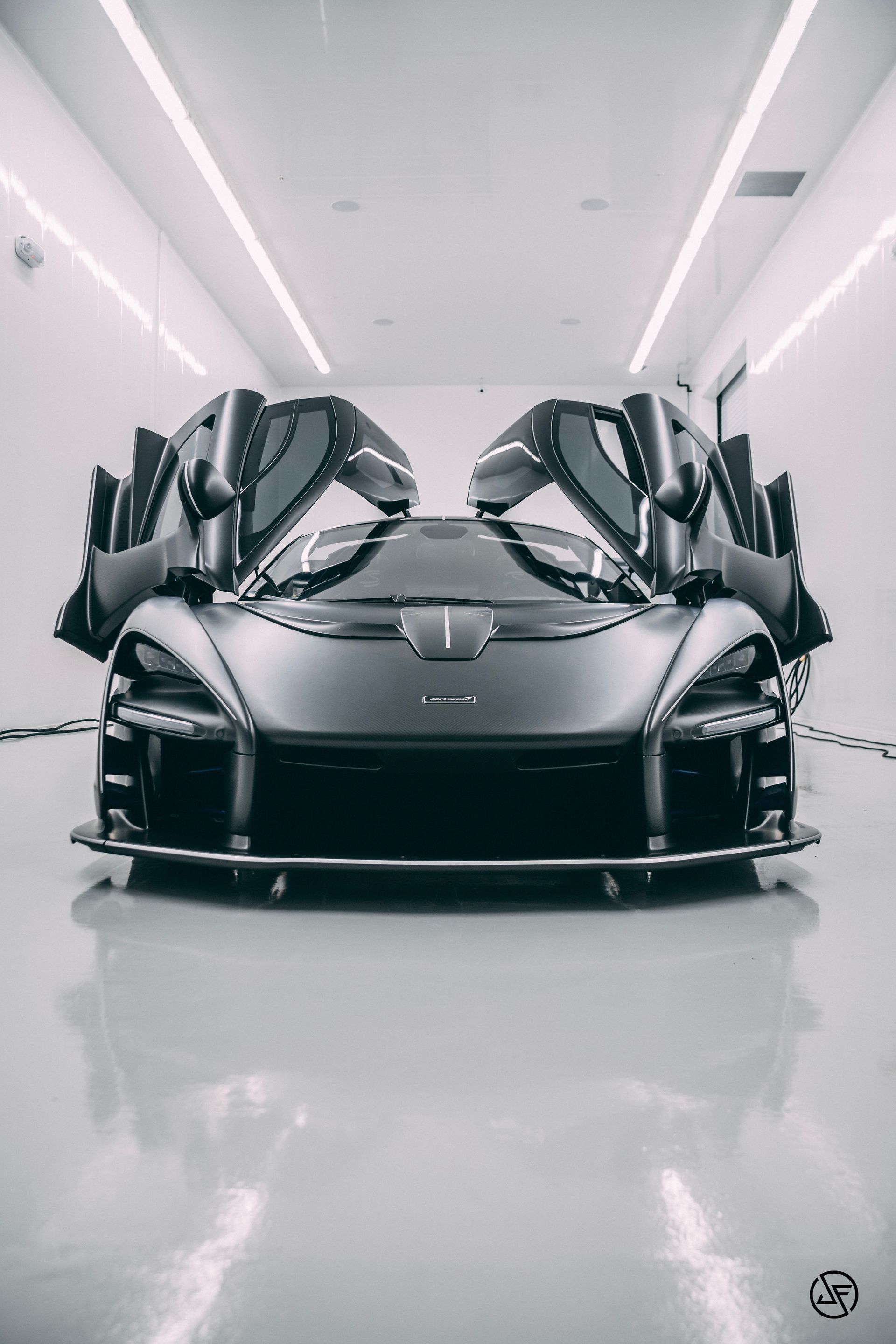 Black McLaren Senna with doors open in a bright, white garage.
