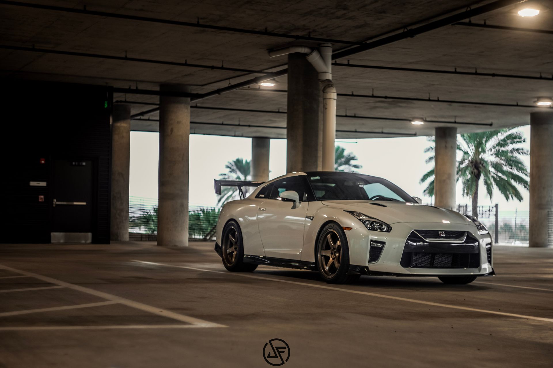 White Nissan GT-R sports car parked in a concrete parking garage with palm trees visible in the background.