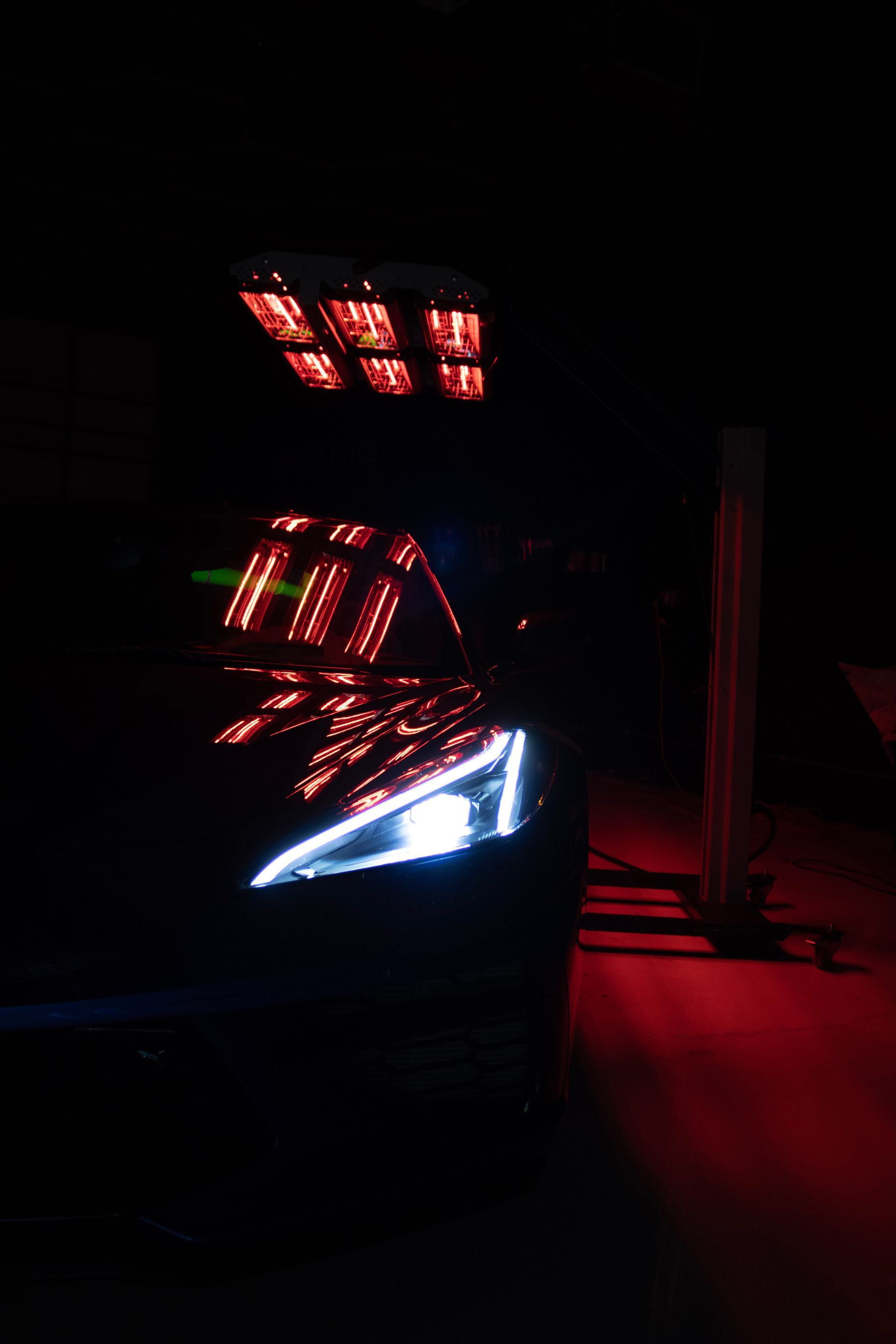 Black car front with white headlights under red lights at night.