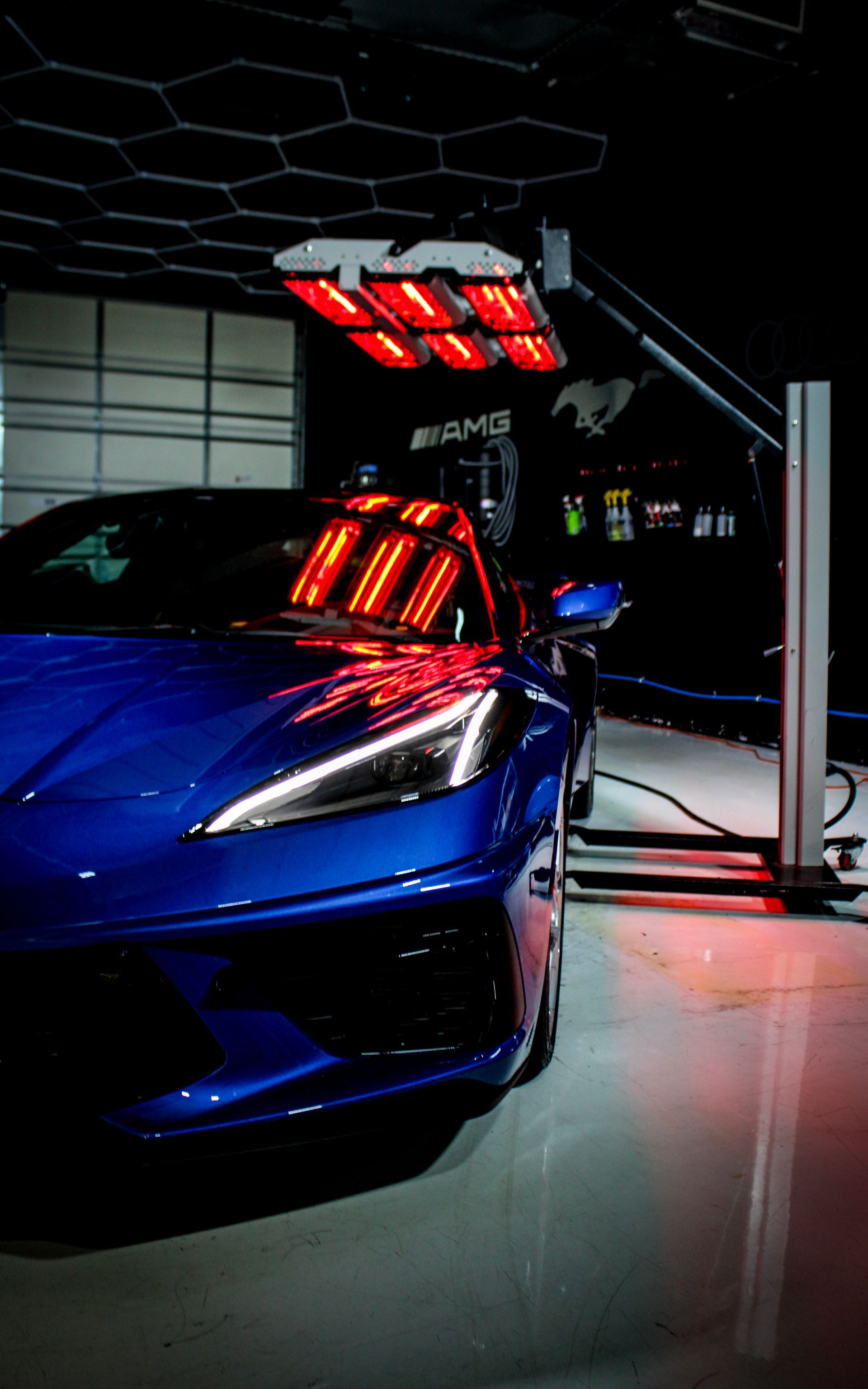 Blue sports car under infrared lights in a garage; lights reflect off the car's hood.