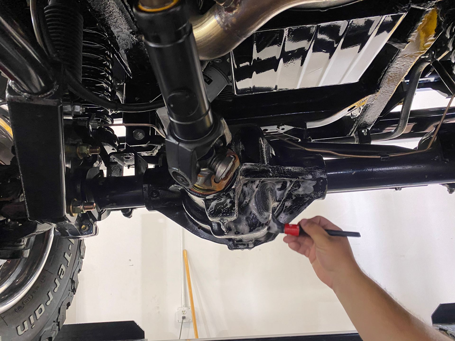 A person cleaning the underside of a black vehicle's rear axle with a brush.