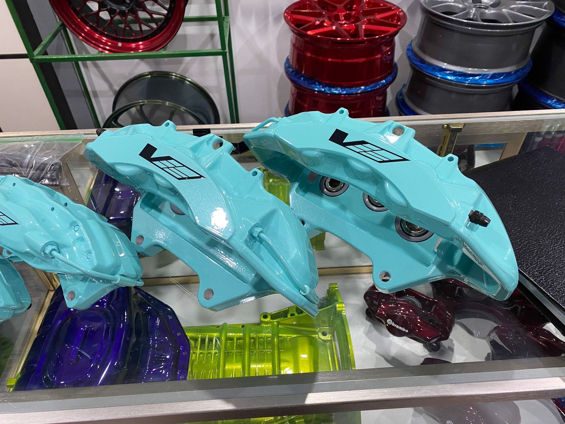 Bright teal brake calipers on display, with other colored car parts in the background.