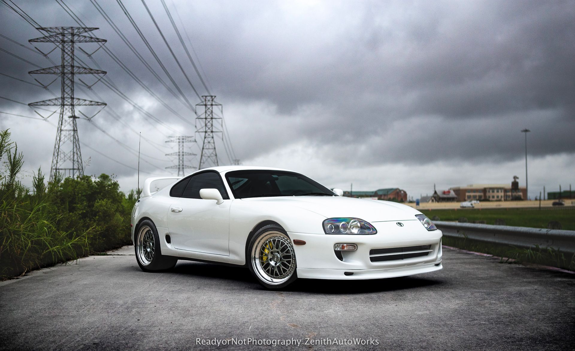 White Toyota Supra sports car parked by road under cloudy sky and power lines.