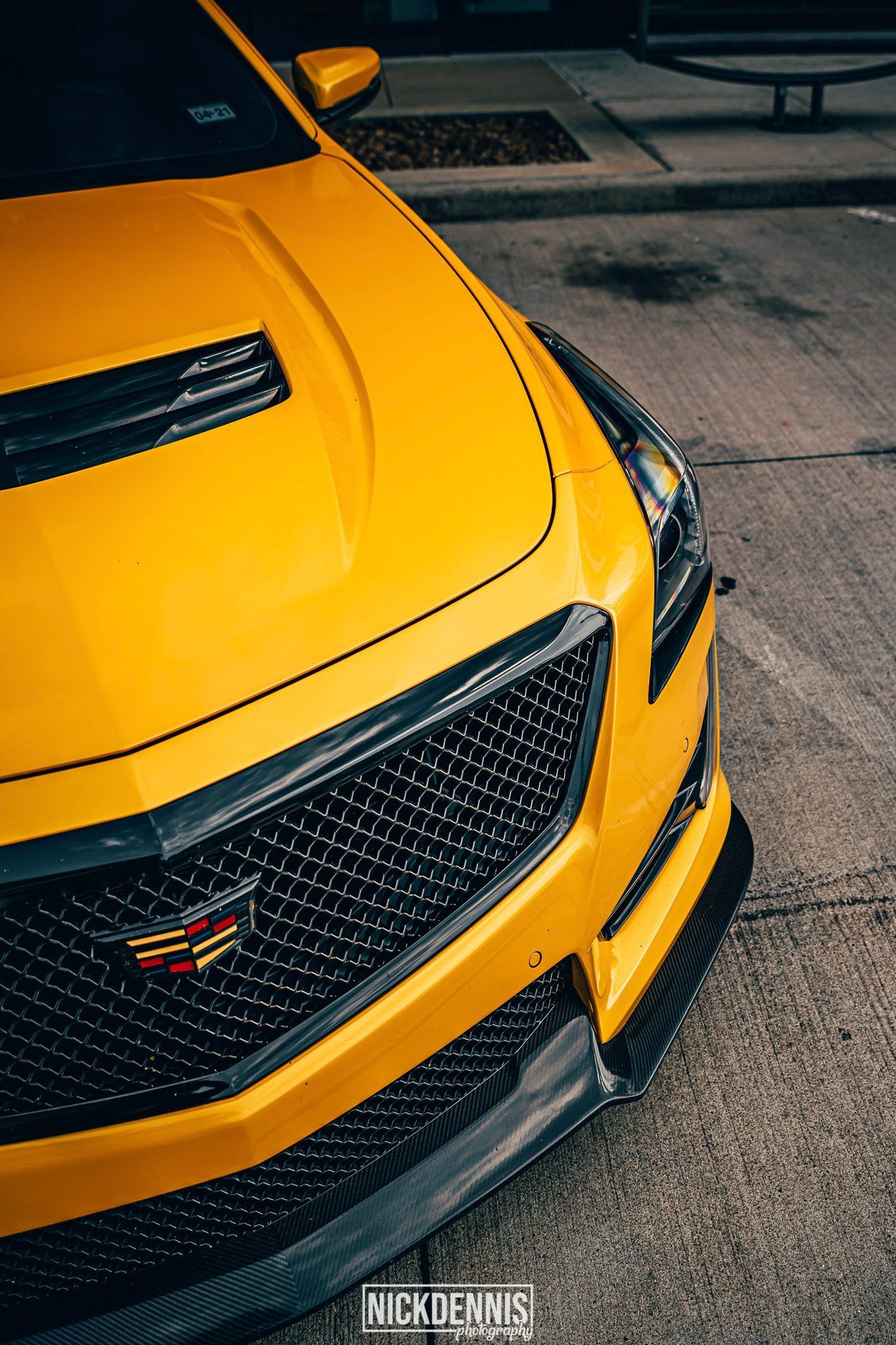 Bright yellow Cadillac CTS-V, close-up of front grill and hood scoop.  Carbon fiber accents. Parked on asphalt.