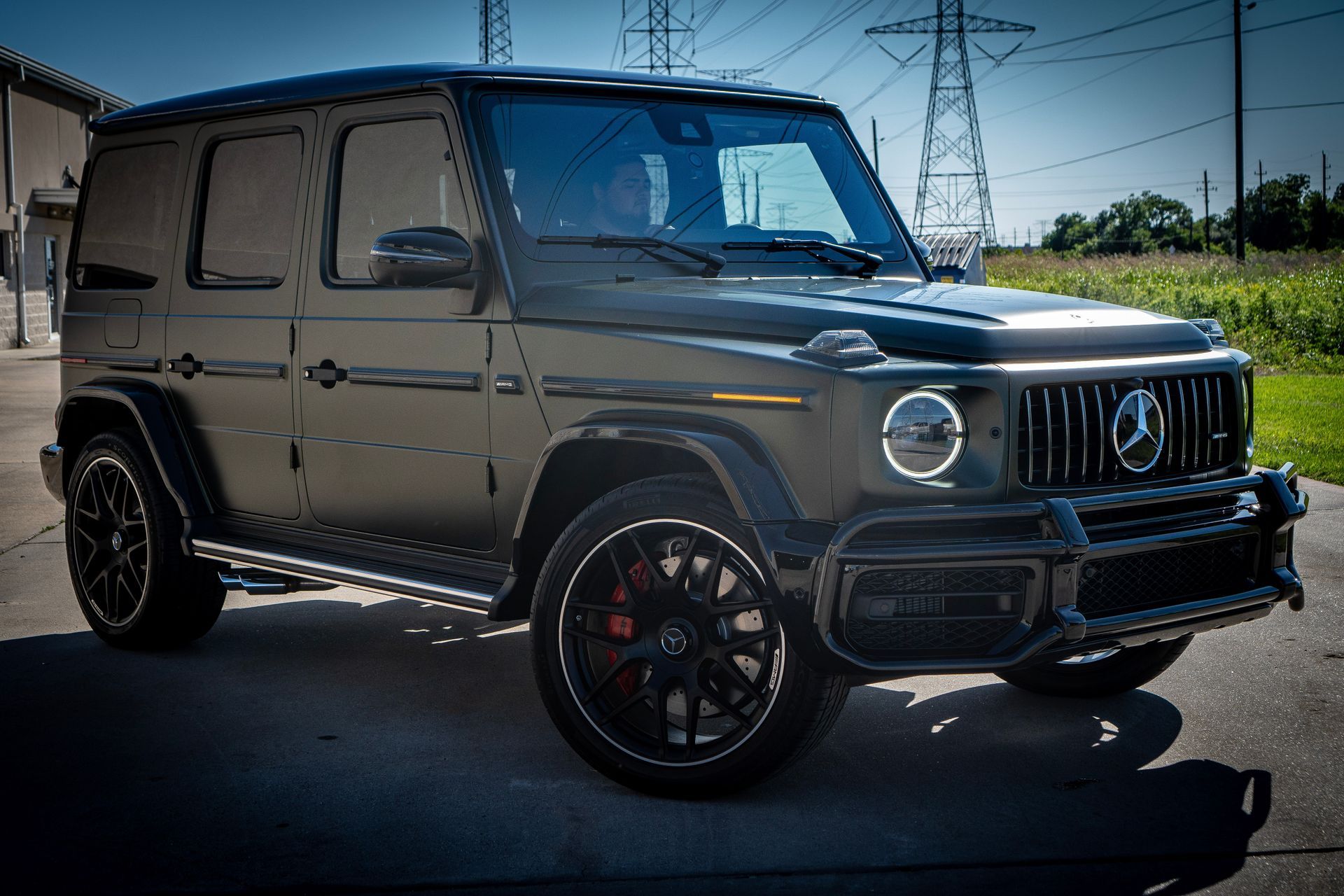 Black Mercedes-Benz G-Class SUV parked on asphalt. It has black rims and red brake calipers. Utility poles are in the background.