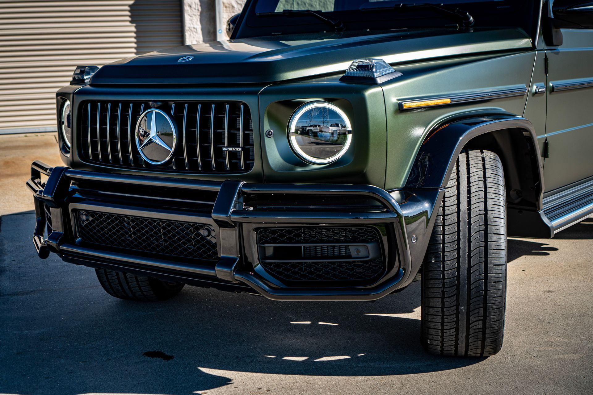 Green Mercedes-Benz G-Class SUV, front view, black grill and bumper, on pavement.
