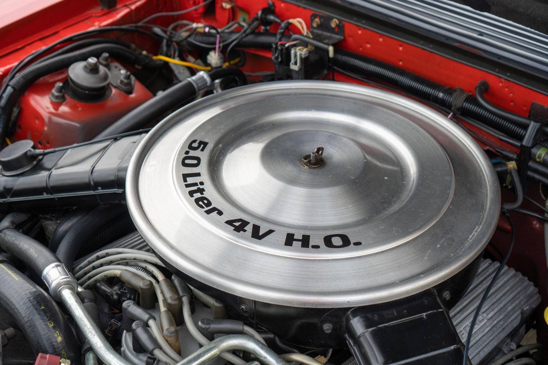 Close-up of a red car engine with a silver air cleaner cover that reads 