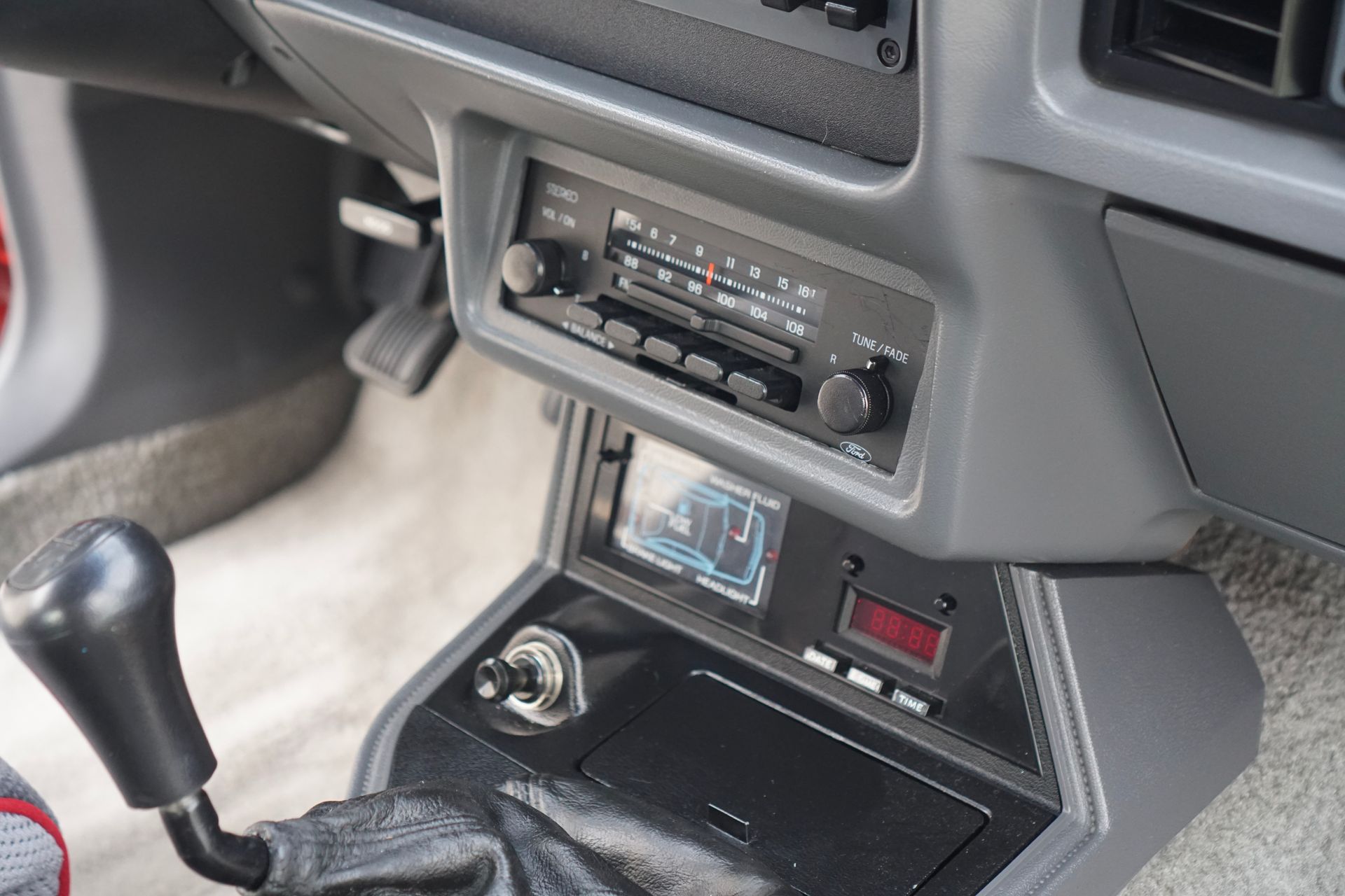 Dashboard of a vintage car with a radio, gear stick, and aftermarket electronics. Gray and black interior.