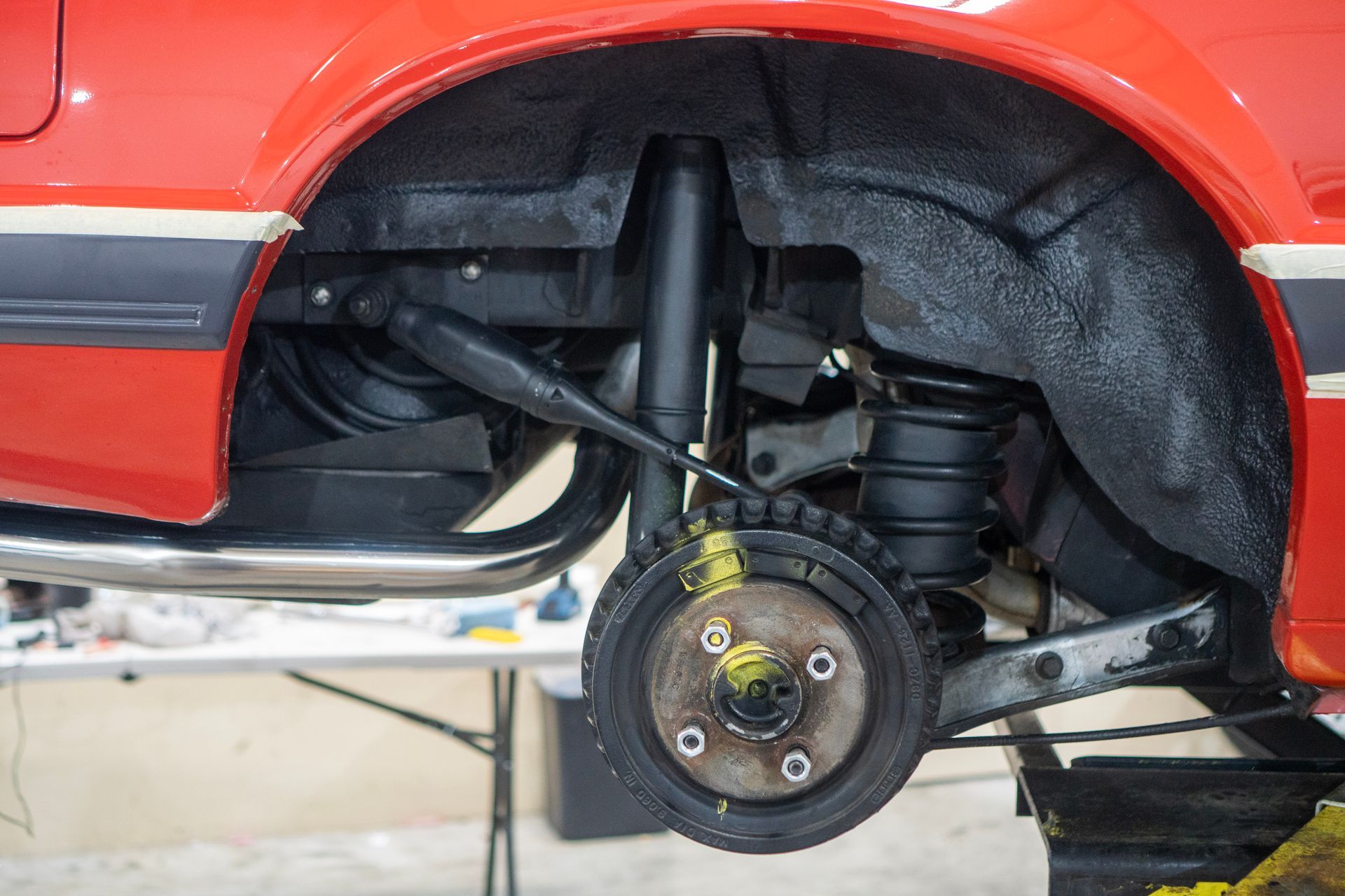 Rear suspension of a red car with a visible shock absorber, spring, and wheel hub.