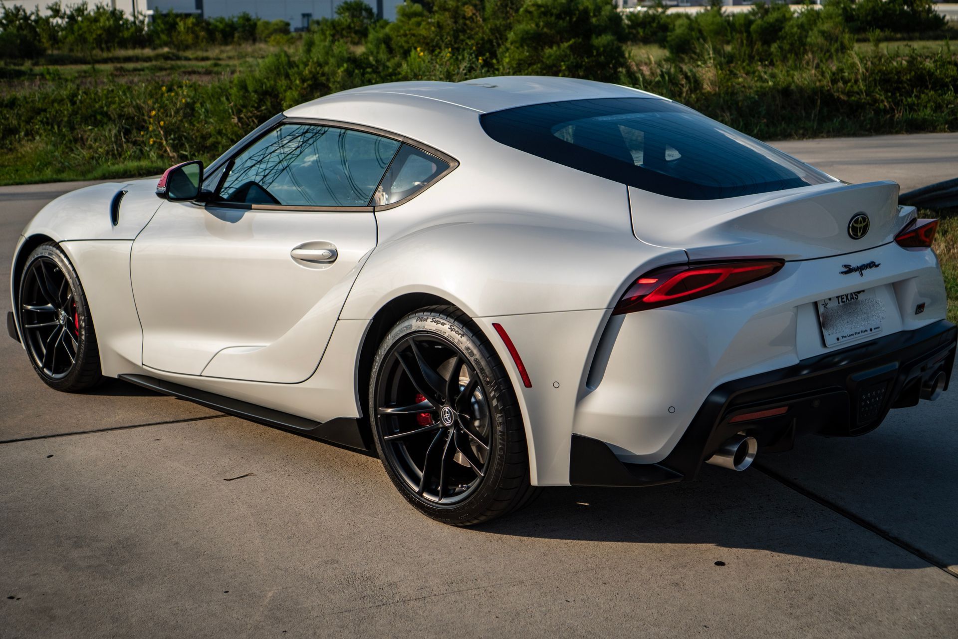 White Toyota Supra sports car on asphalt, black wheels, side view.