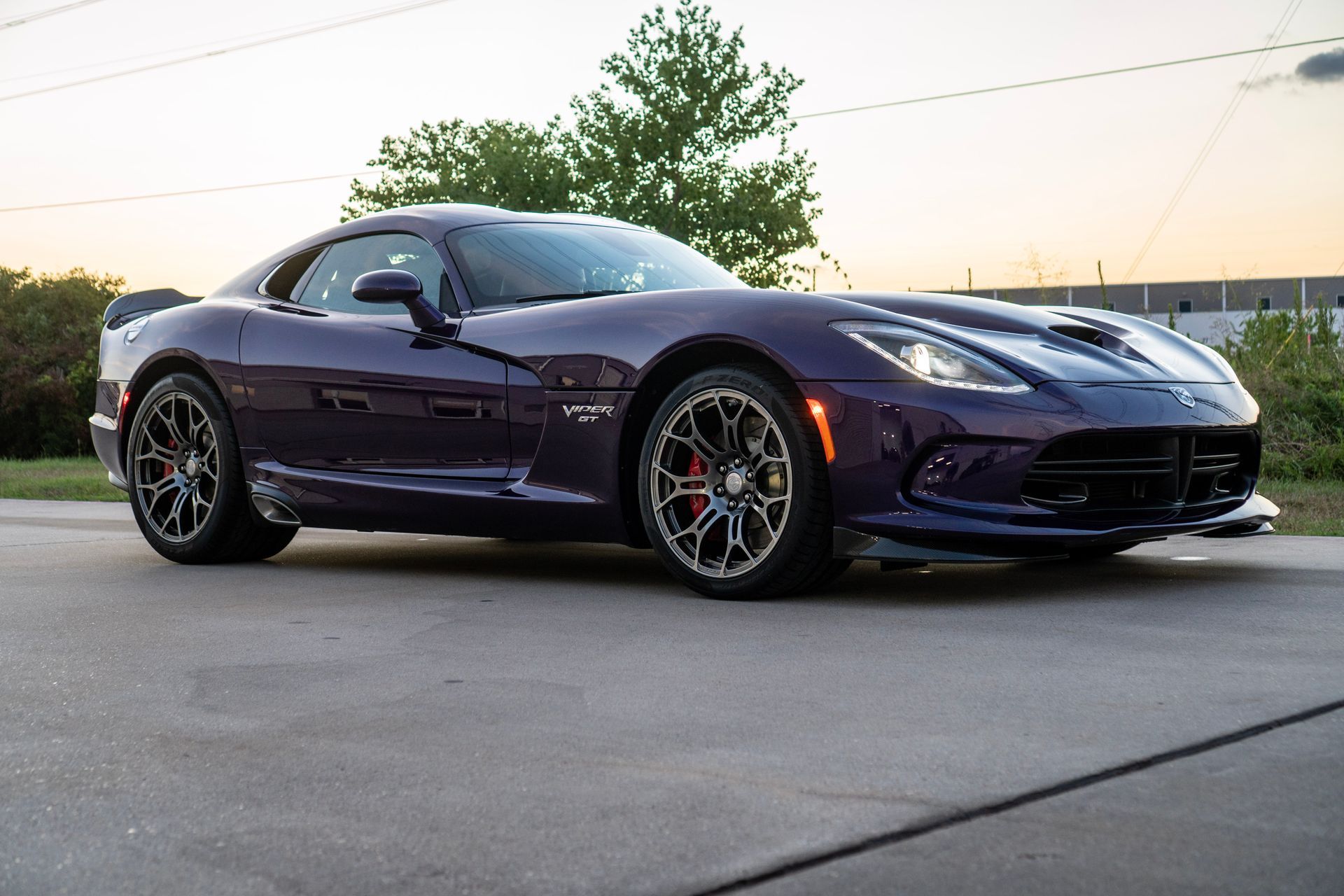Dark purple Dodge Viper sports car parked on asphalt, setting sun in the background.
