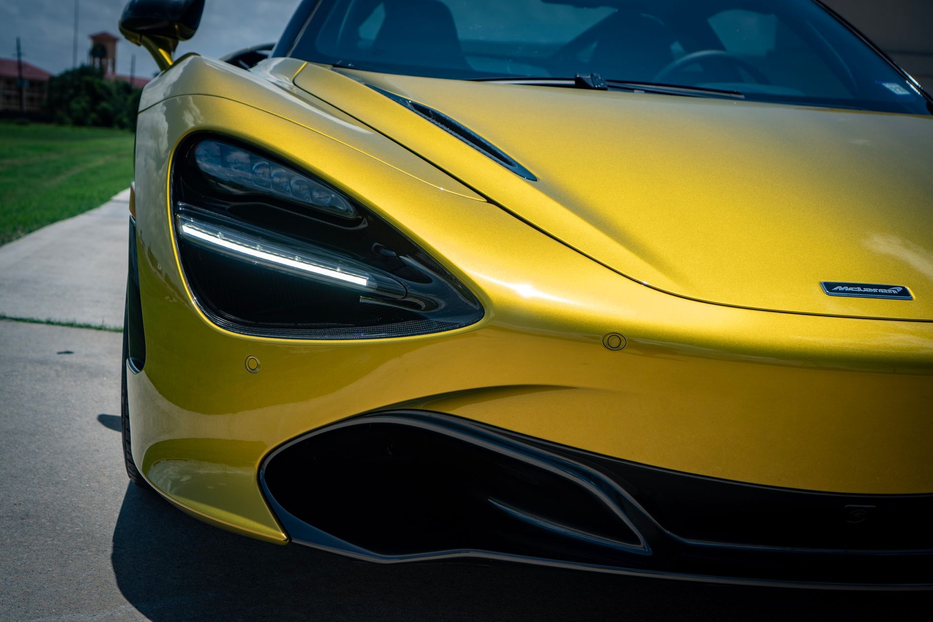 Yellow McLaren sports car, front view, parked on a paved surface with grass in background.