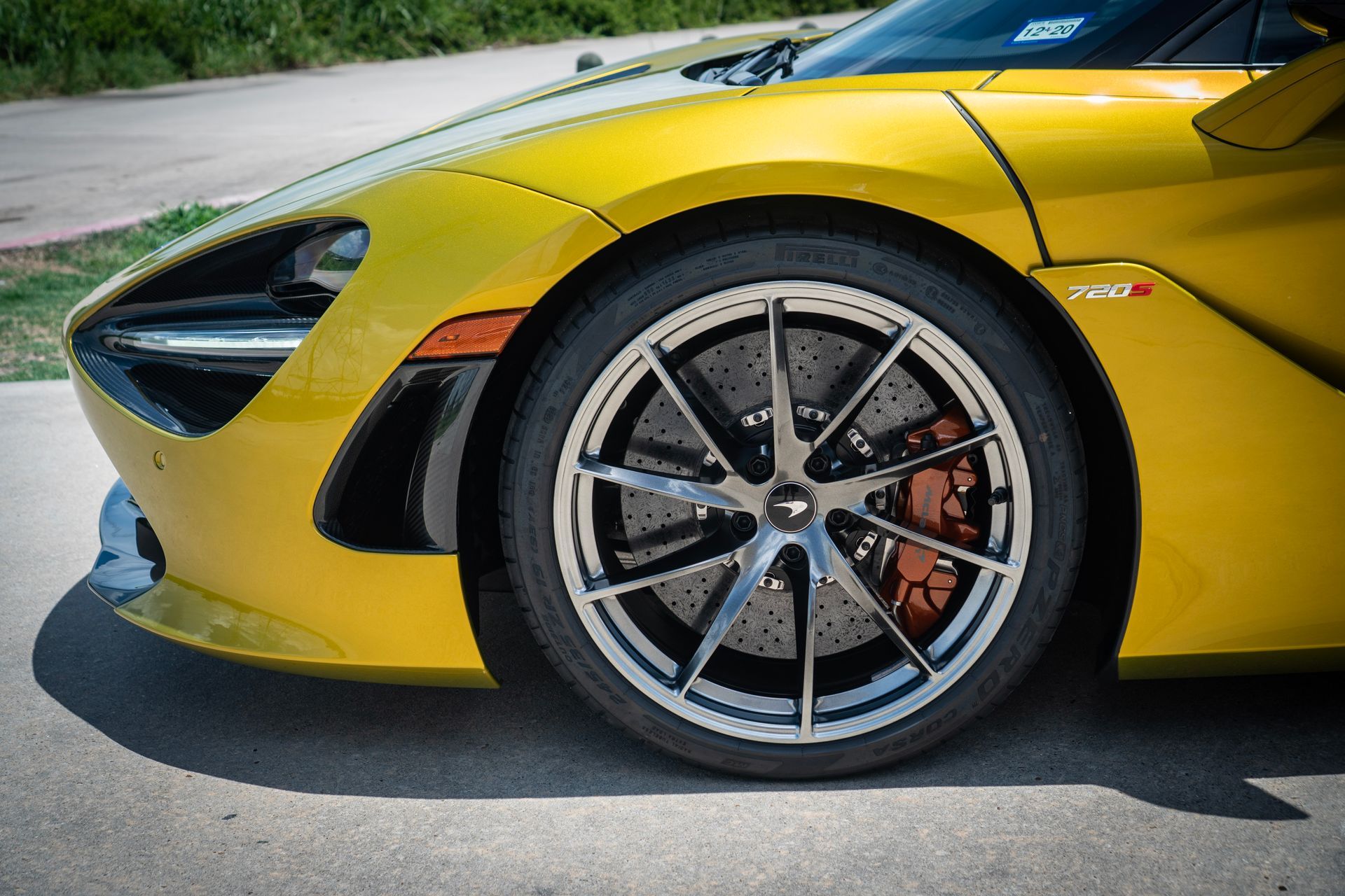 Yellow McLaren sports car front wheel, silver rims, orange brake calipers.
