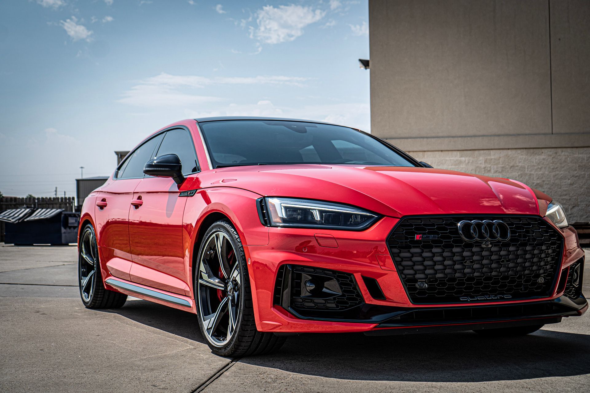 Red Audi RS5 coupe parked on pavement with building in background.