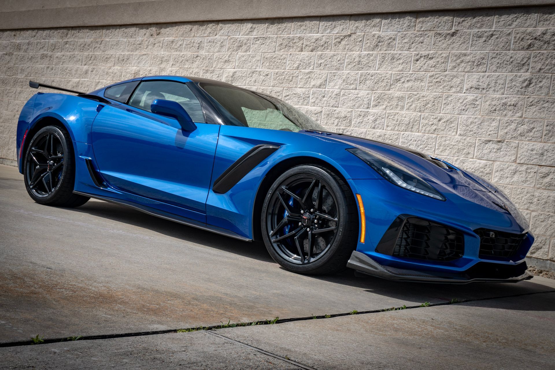 Blue Chevrolet Corvette ZR1 sports car parked in front of a brick wall.