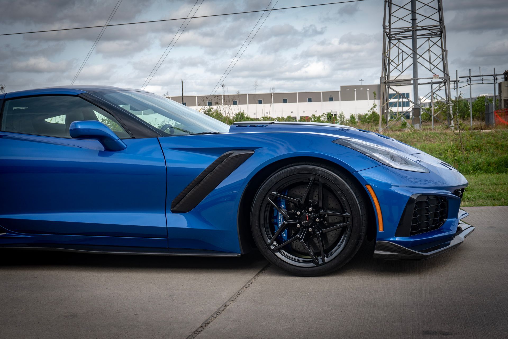 Blue sports car parked on concrete, black wheels, dark accents, overcast sky.