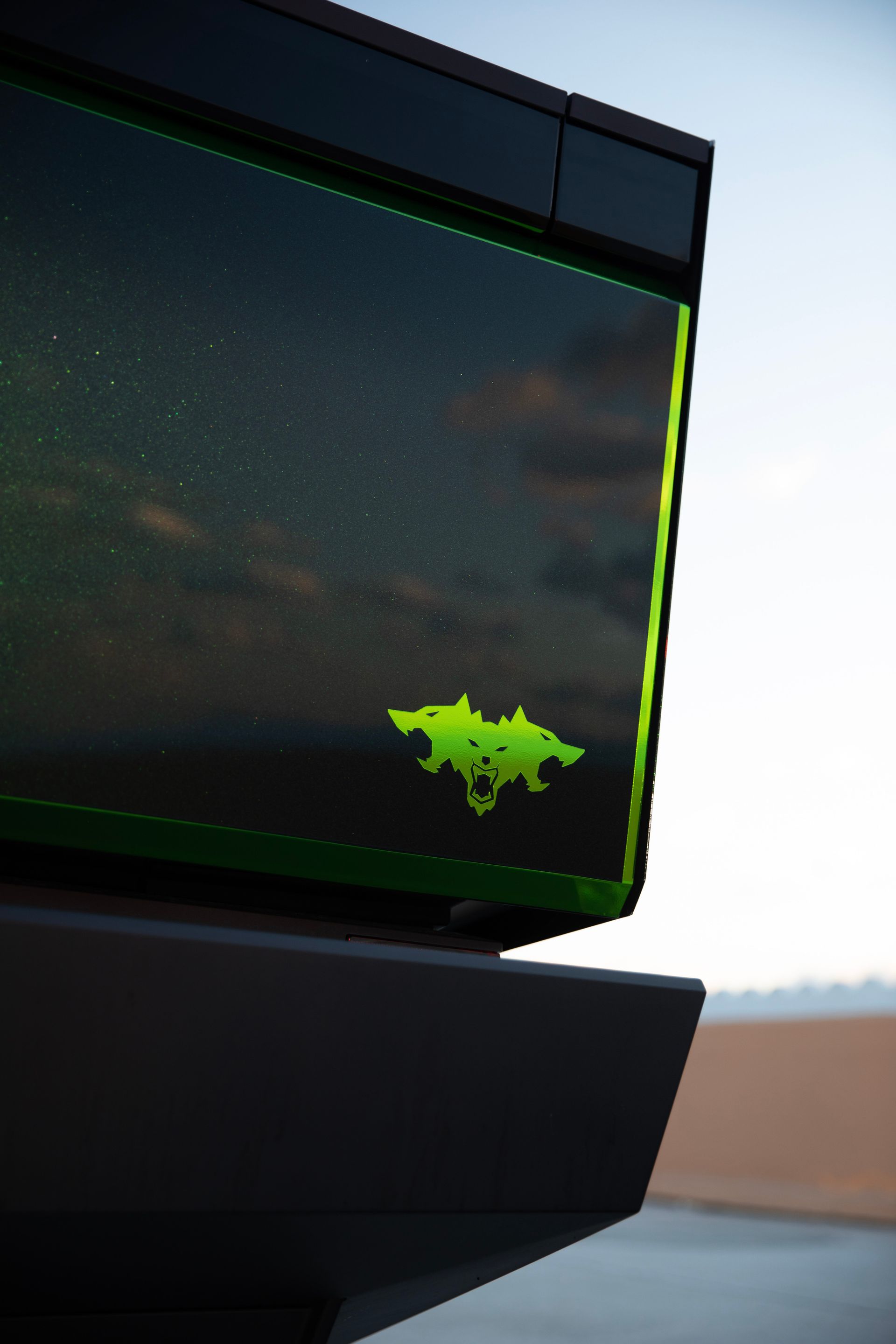 Black and green electronic device with a glowing green bat-like symbol on the side, against a dark sky.