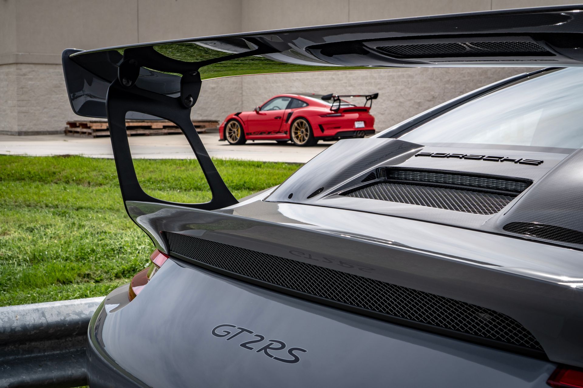 Gray Porsche GT2 RS with large wing; red Porsche in background.