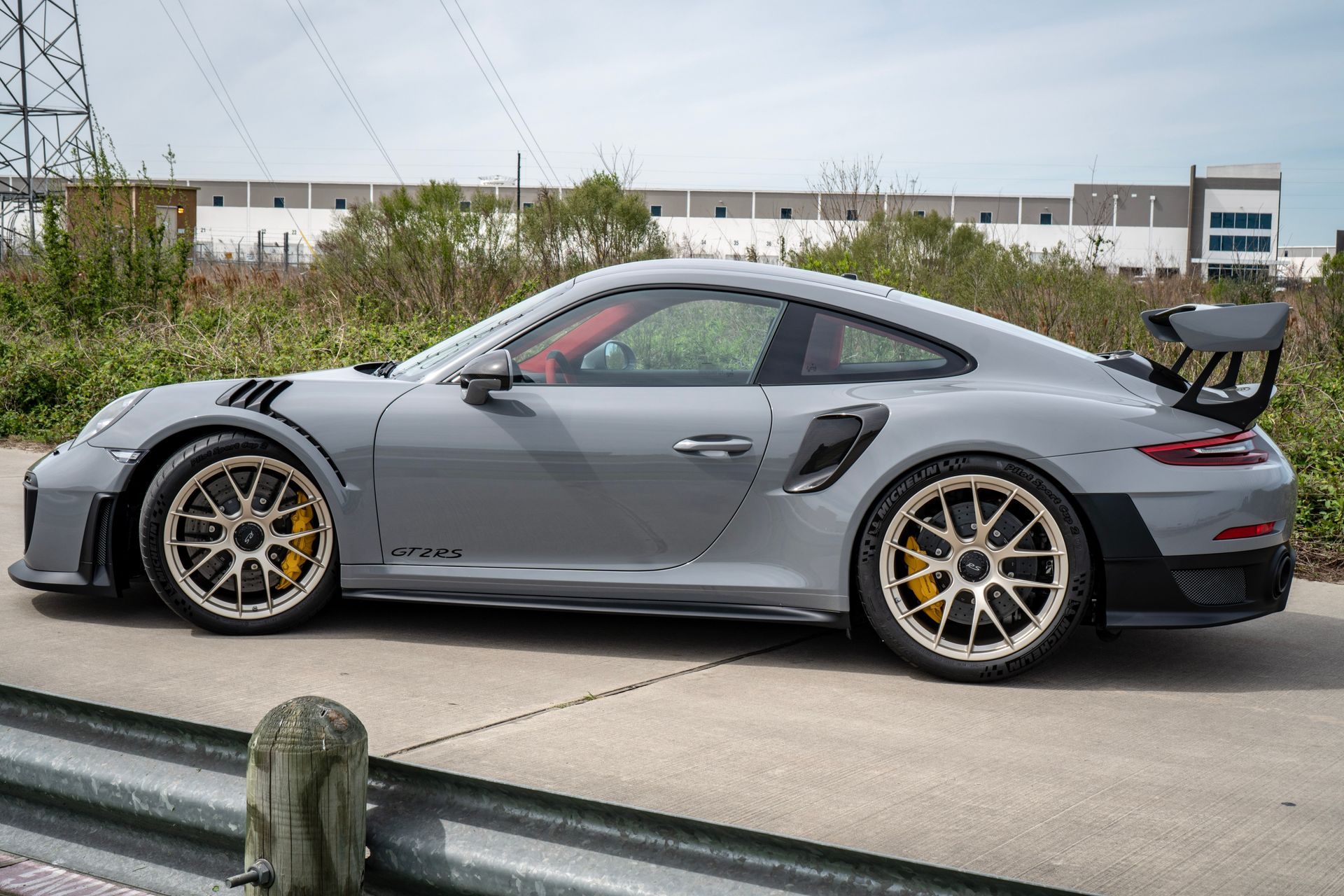 Gray Porsche 911 GT2 RS coupe with gold wheels on a paved road, daytime.