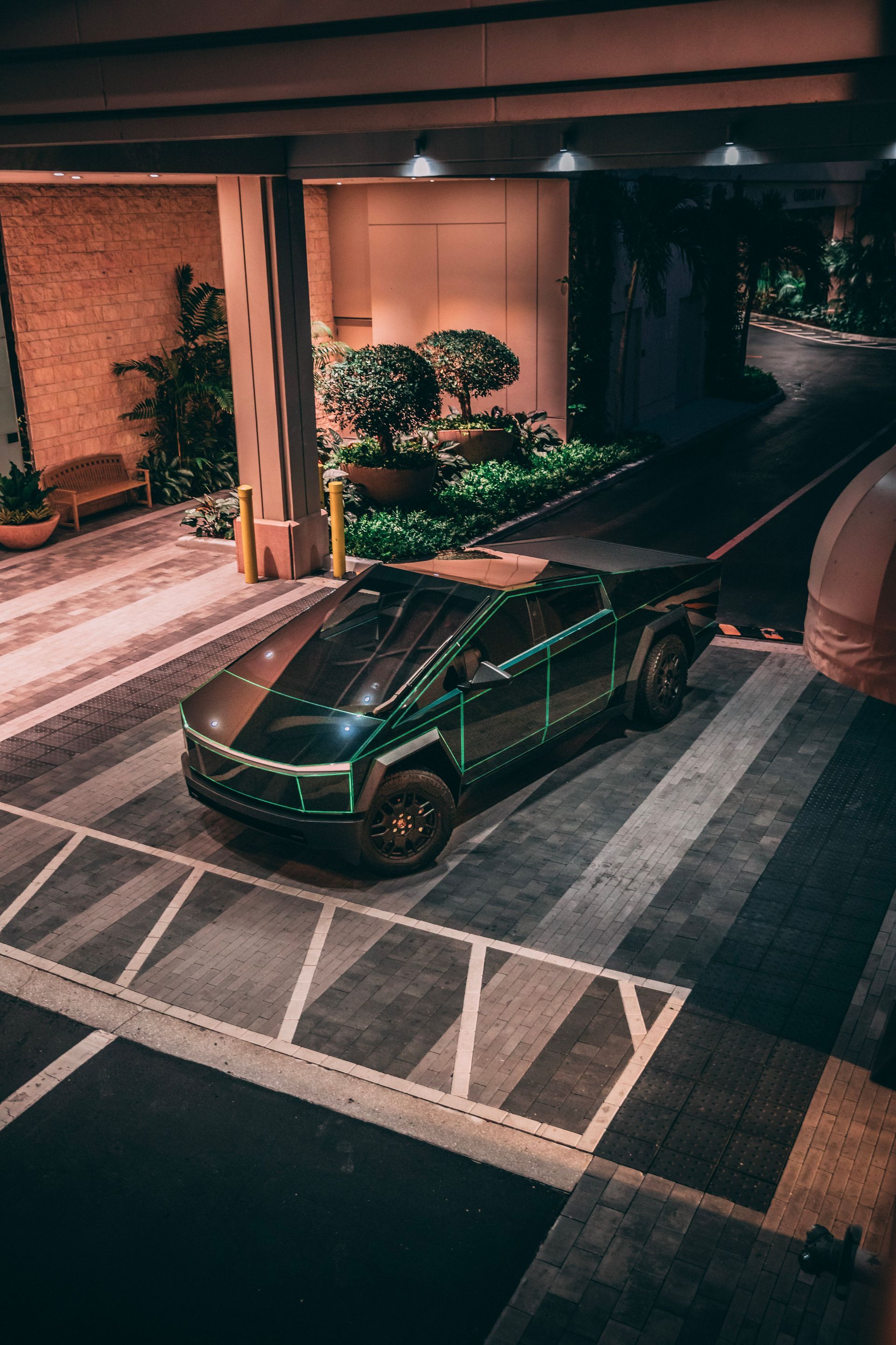 Green Tesla Cybertruck parked under a building overhang at night, with dark, angular design.