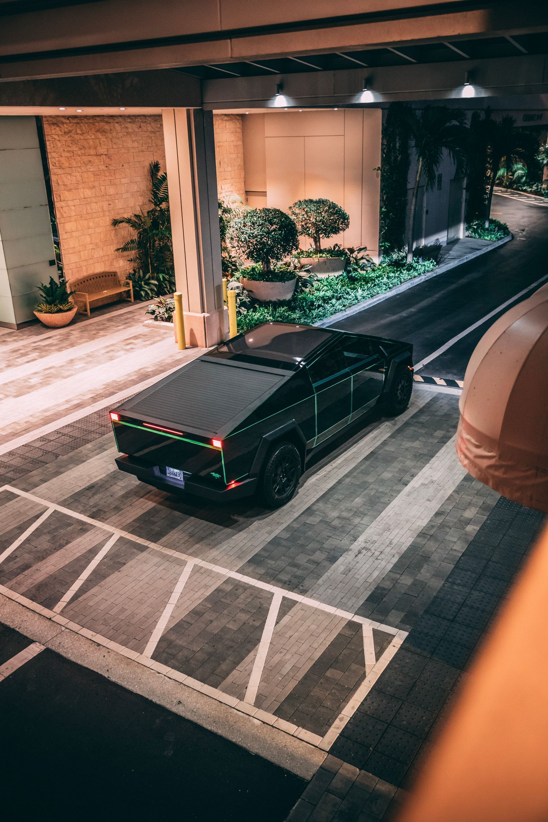 Black Tesla Cybertruck parked under a building overhang with greenery, lit by nighttime lights.