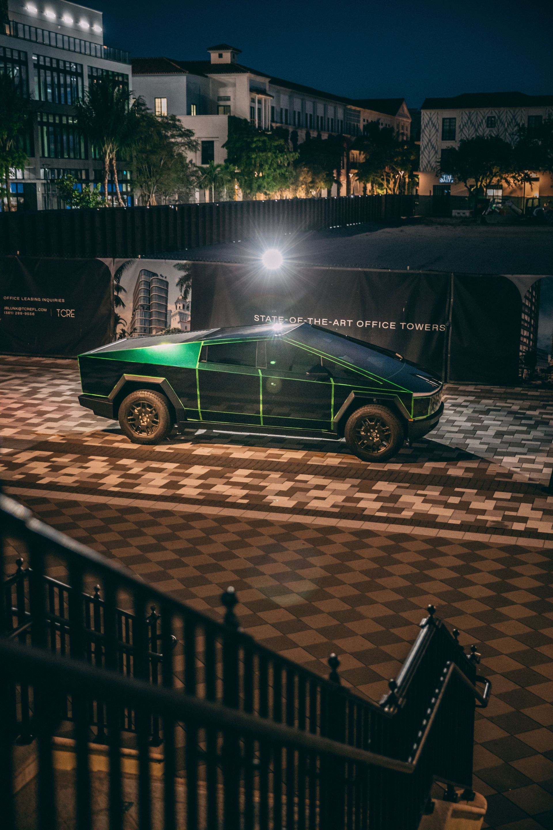 Tesla Cybertruck with green wrap parked on cobblestones at night, near stairs.