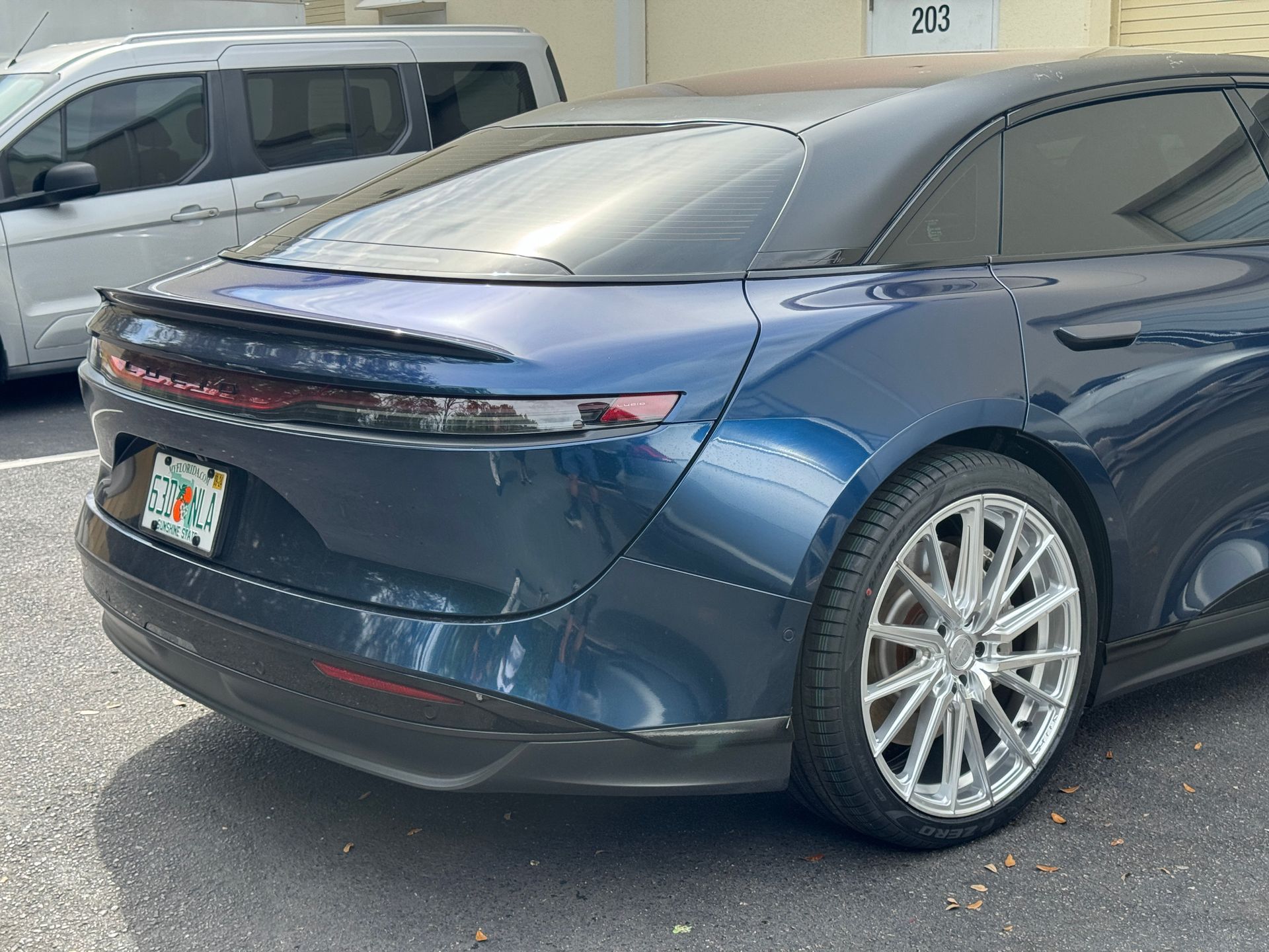 Blue Lucid Air electric car with chrome wheels, parked near a building with the number 213.