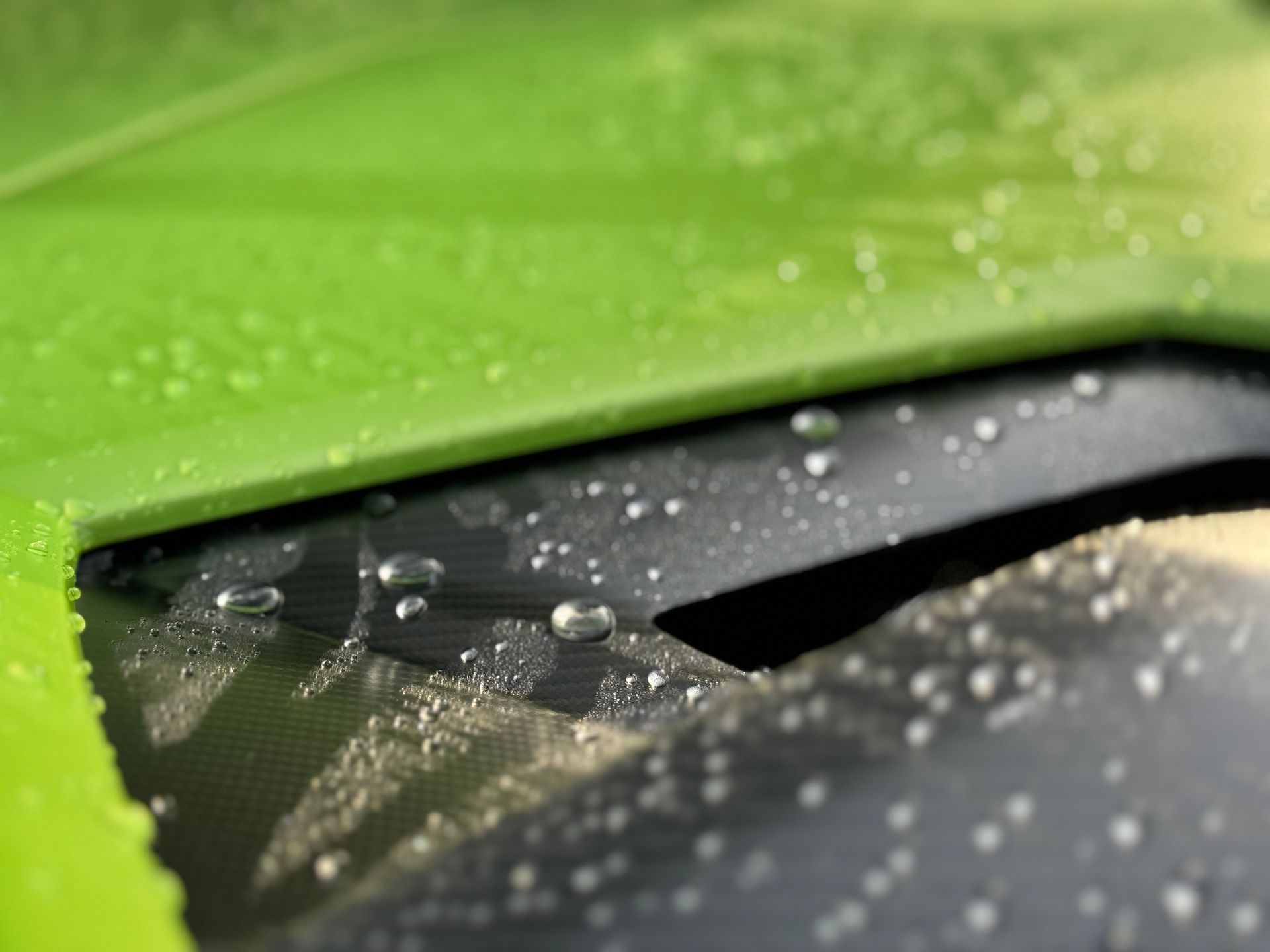 Green car hood close-up with water droplets on the dark, angled surface.