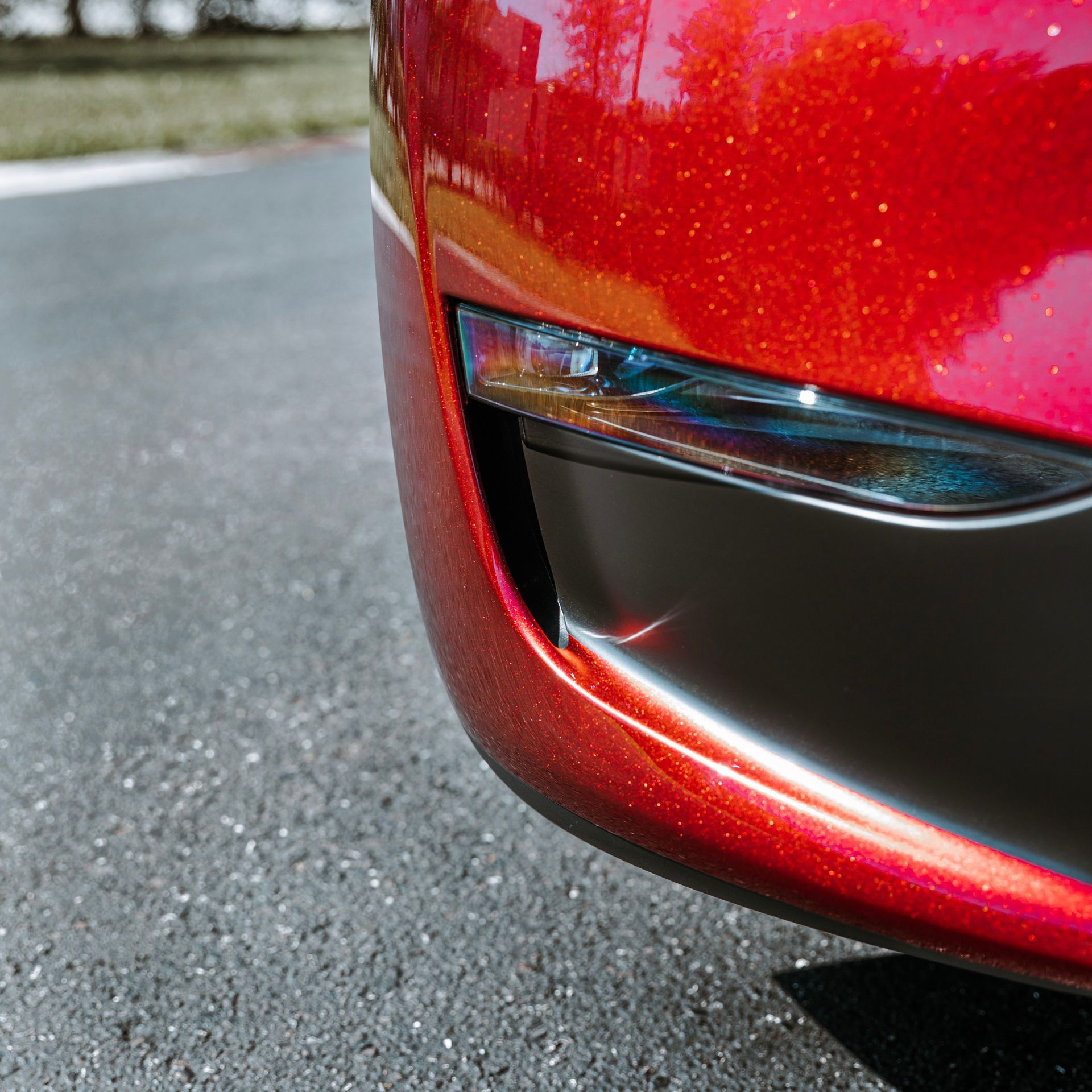 Red car bumper with a black vent; parked on asphalt.