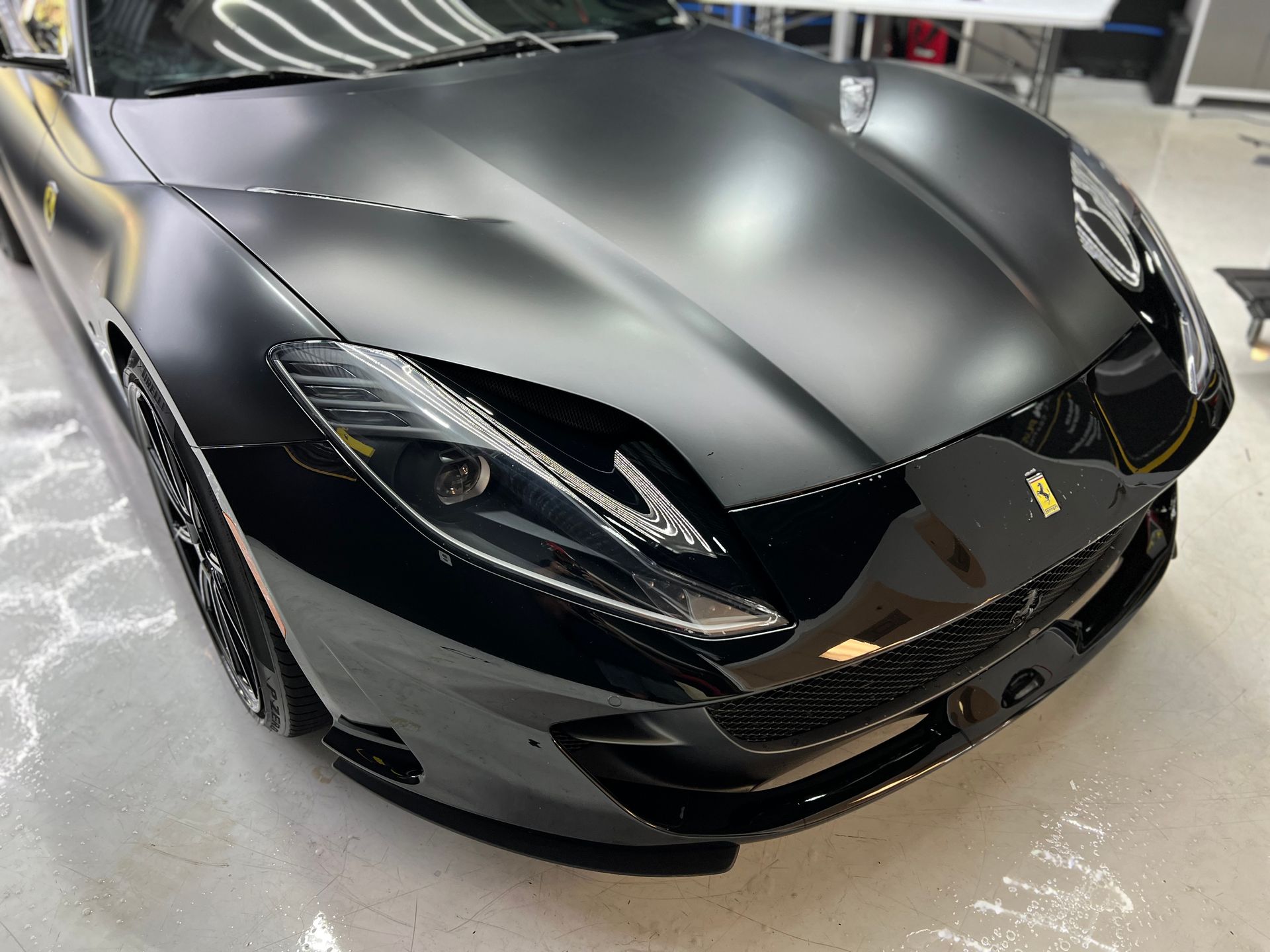 Black Ferrari with matte hood, glossy front, in a garage.