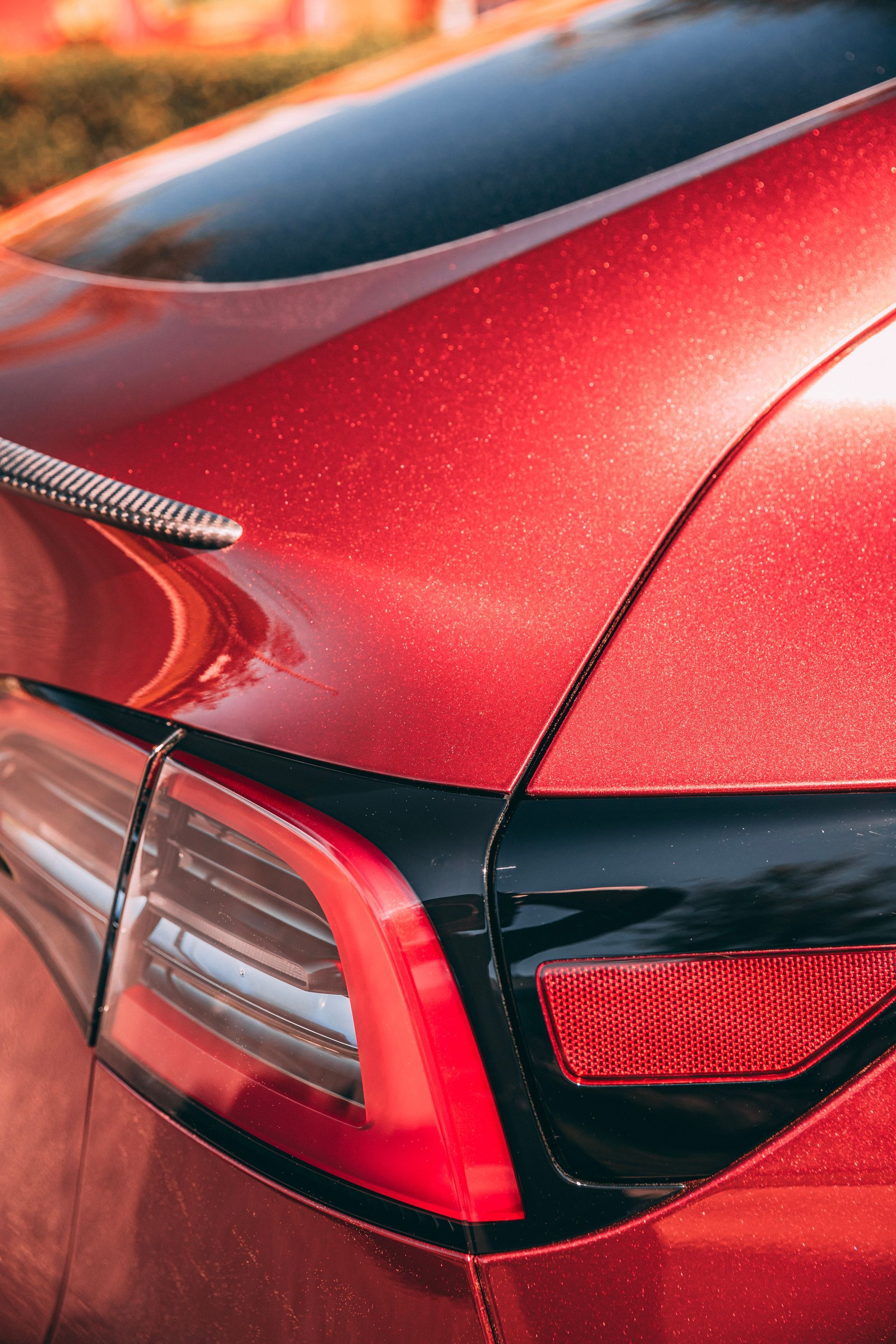 Red Tesla car rear with black trim and tail light.