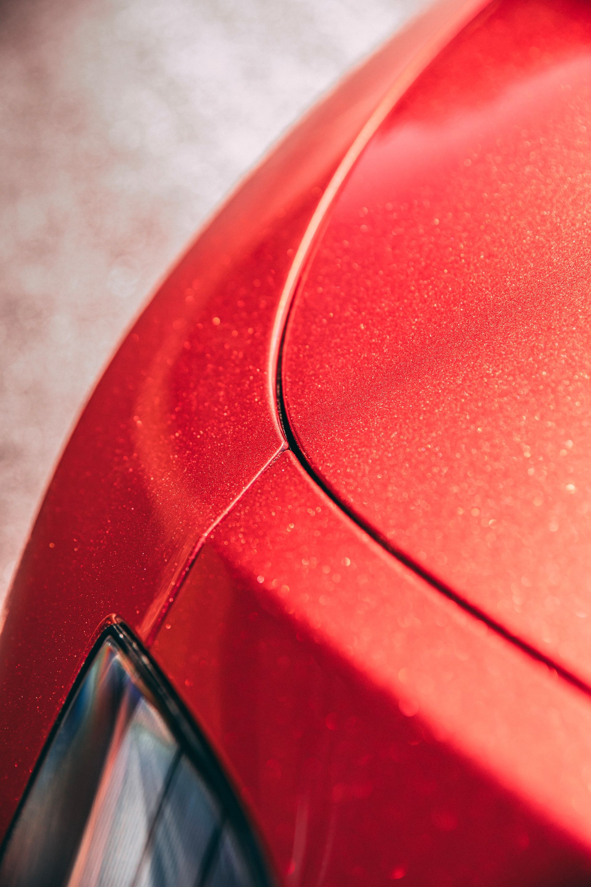 Red car's curved hood and front corner. Dust particles visible.