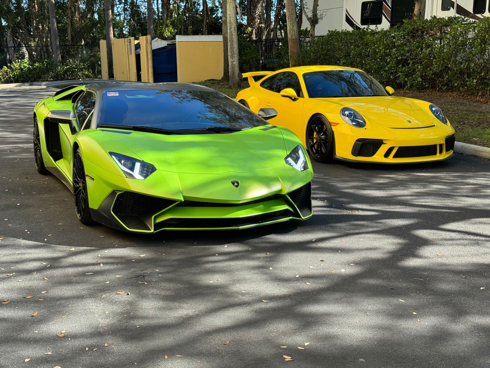 Green Lamborghini and yellow Porsche parked on asphalt.