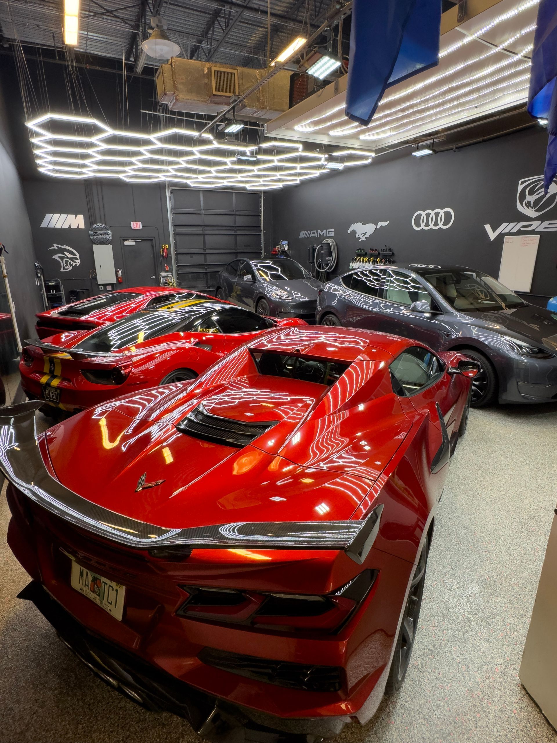 Red sports cars inside a brightly lit garage. Other cars and logos are also visible.