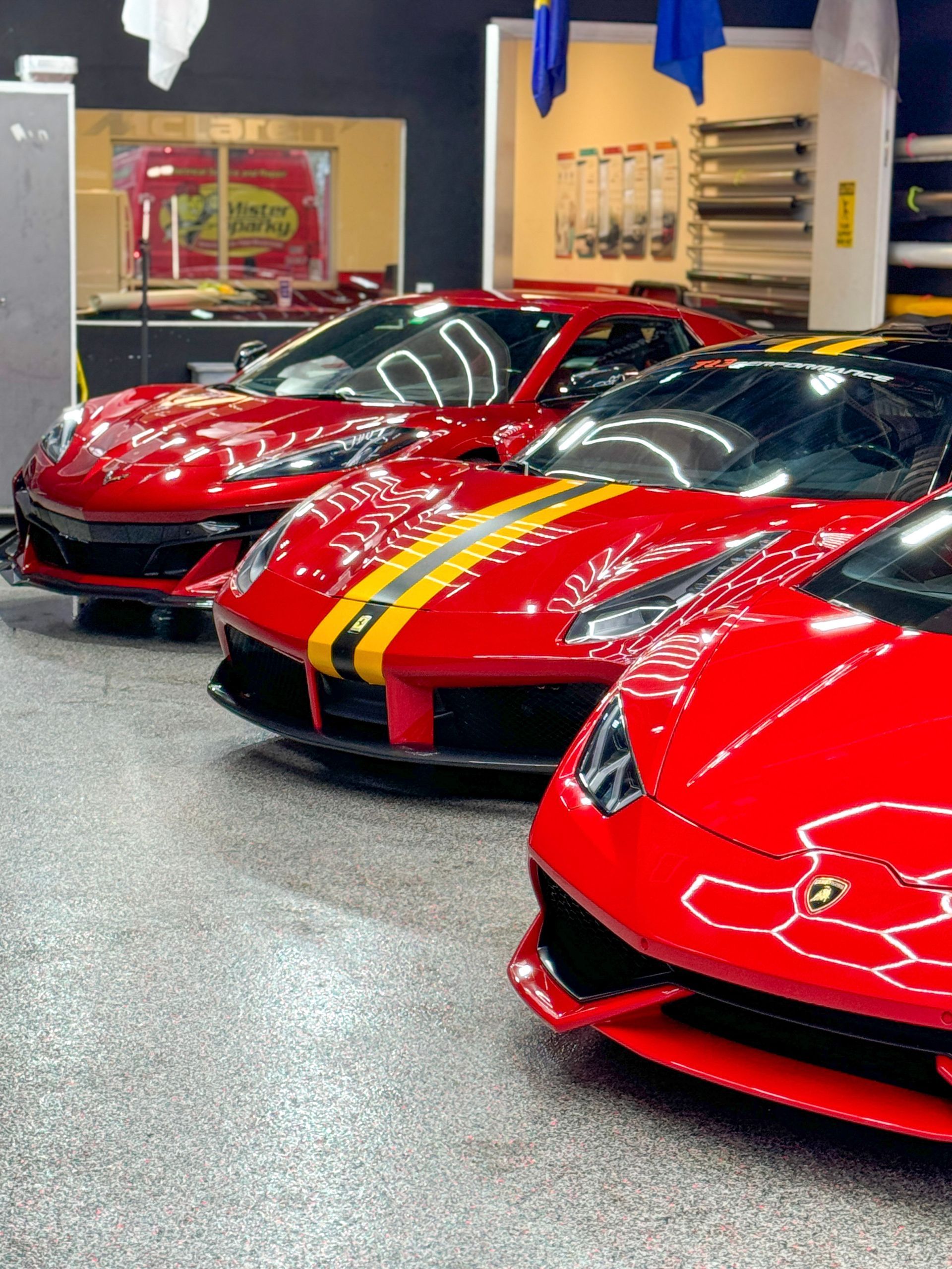 Red sports cars parked inside a garage. One has yellow racing stripes.