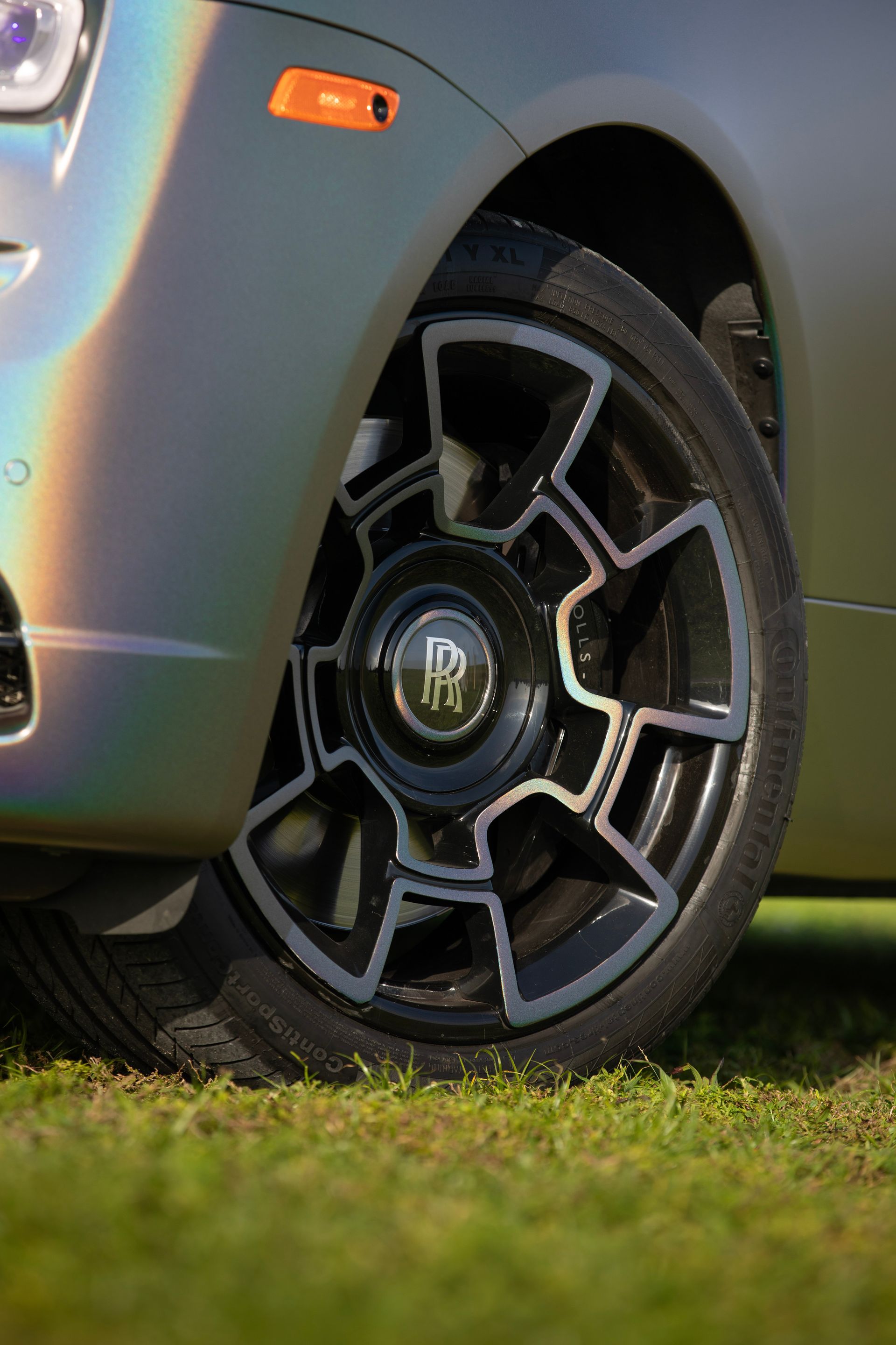 Close-up of a Rolls-Royce car wheel with a black and silver geometric design, parked on grass.