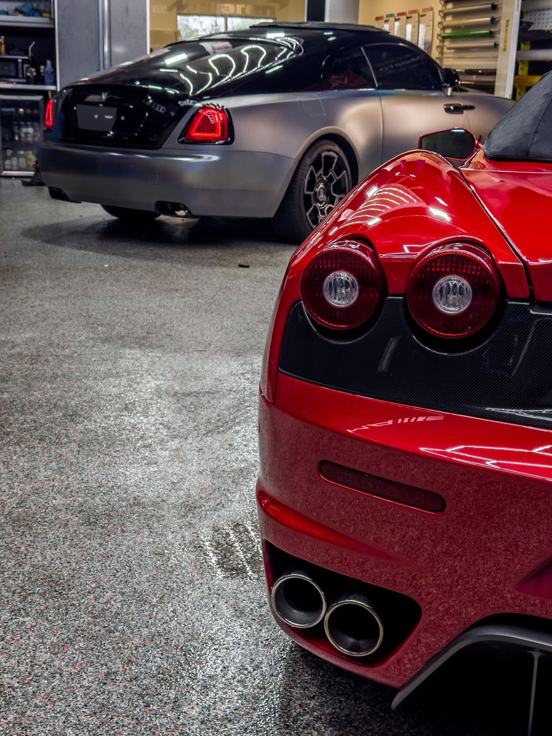 Red Ferrari and gray Rolls-Royce parked in a garage.