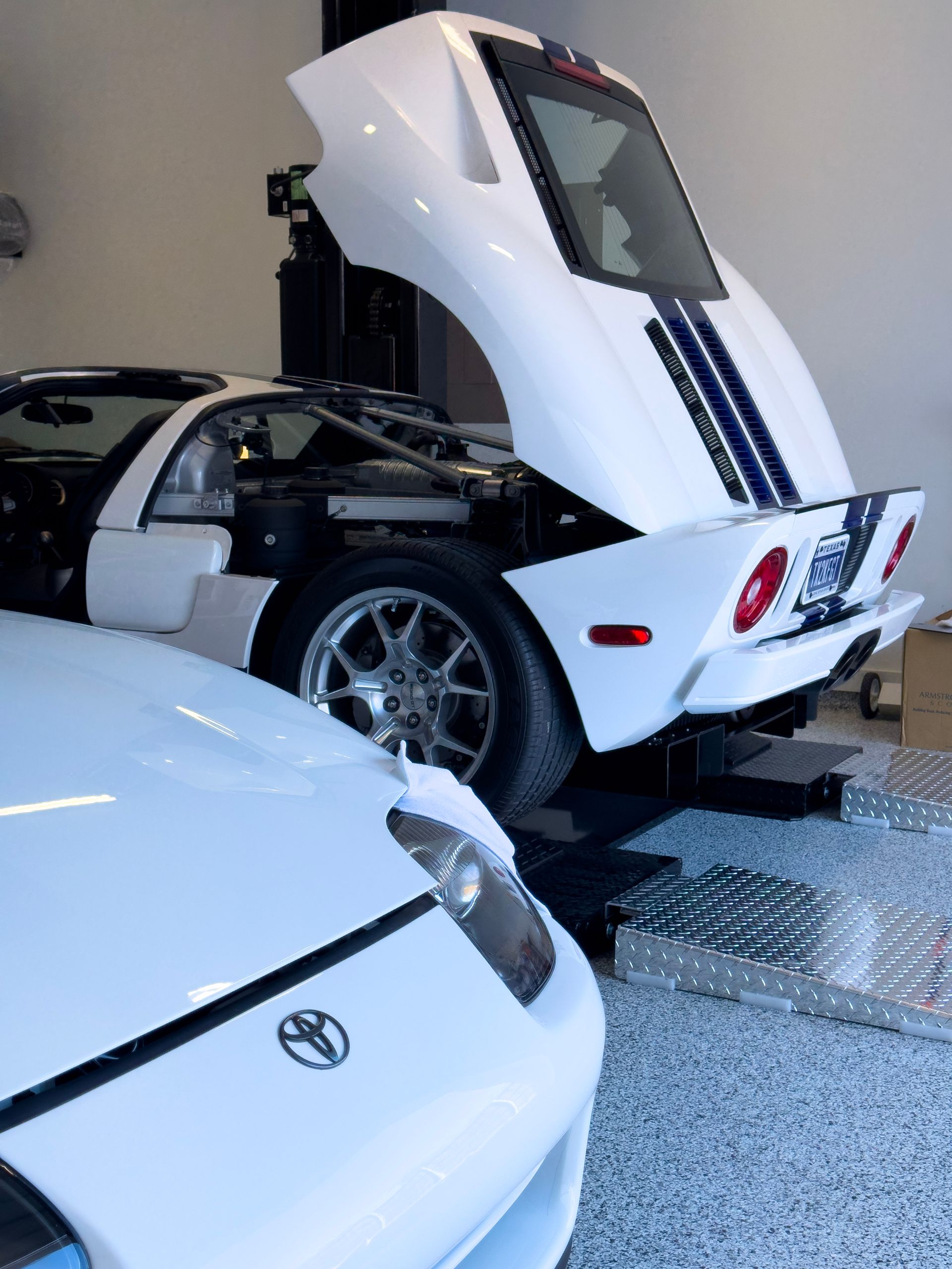 White Ford GT sports car with open rear hood and white sports car in a garage.