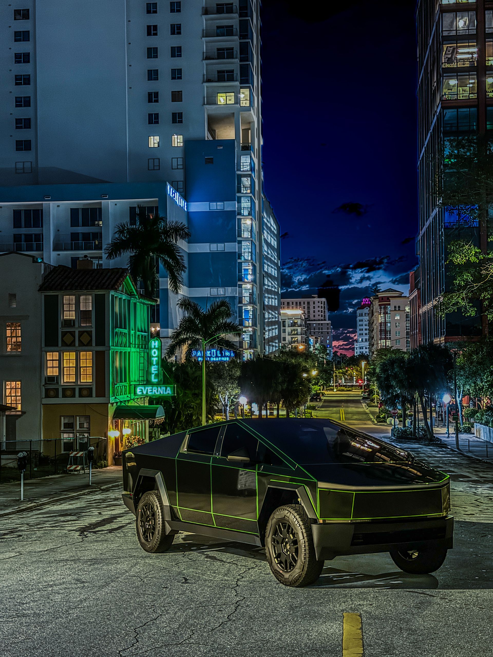 Tesla Cybertruck parked on a cobblestone street at night, with buildings and a neon hotel sign in the background.
