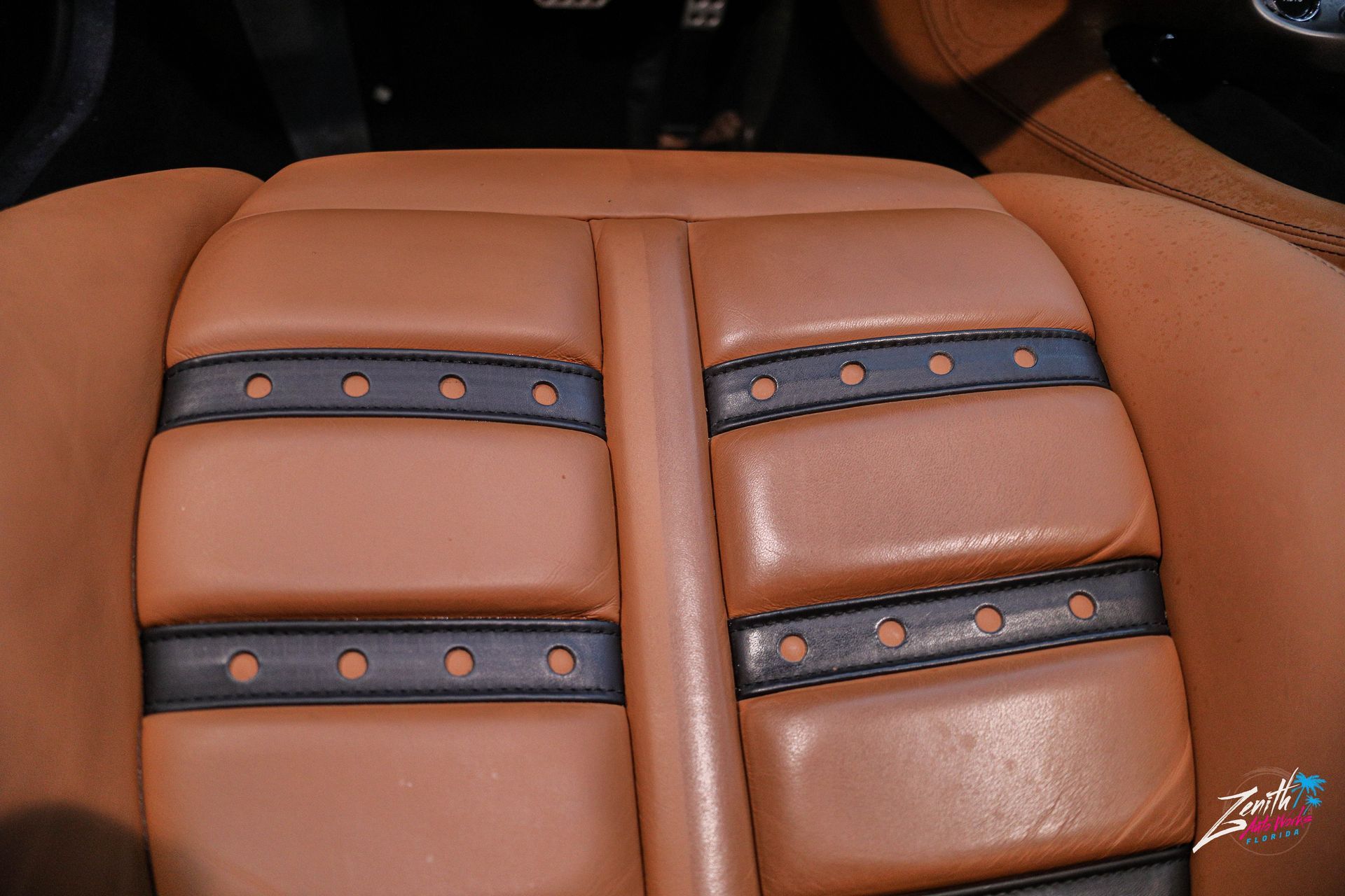 Tan leather car seat with black accents and stitching.