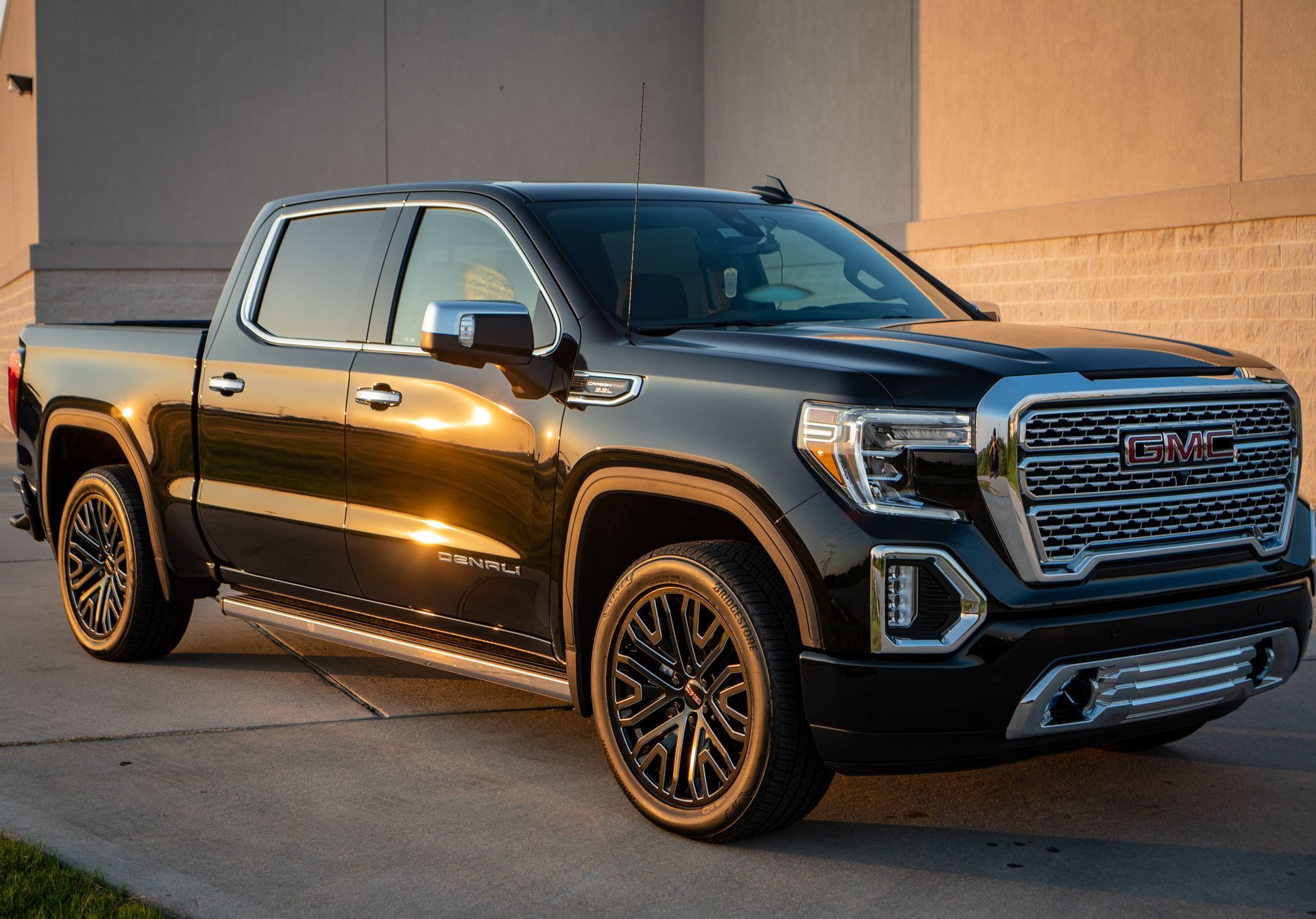 Black GMC Sierra pickup truck parked in front of a building, golden light reflecting on the vehicle.