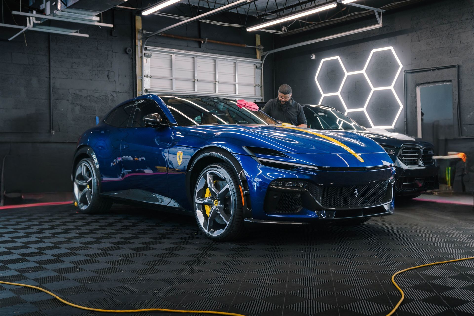 Blue Ferrari SUV in a car detailing bay, person cleaning the hood.