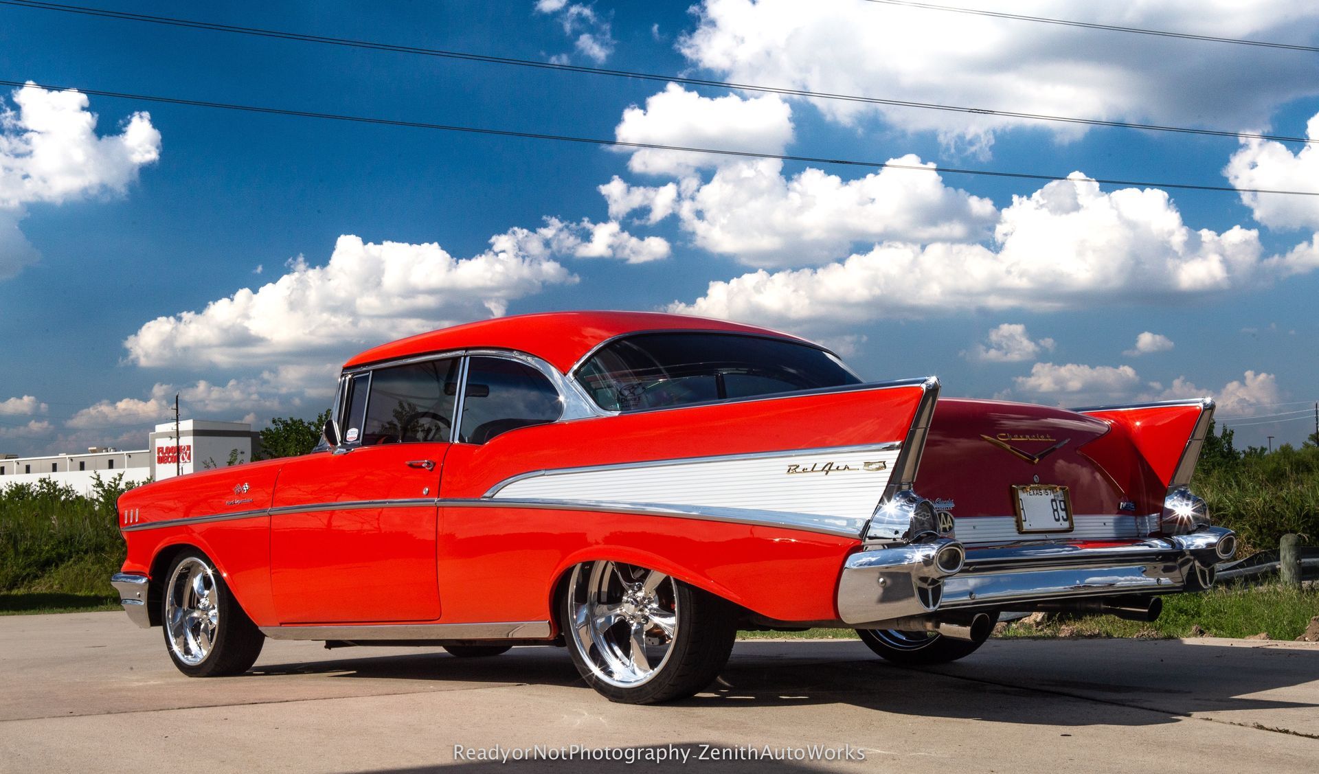 Red classic 1957 Chevrolet Bel Air car with chrome accents parked outside under a blue sky with clouds.