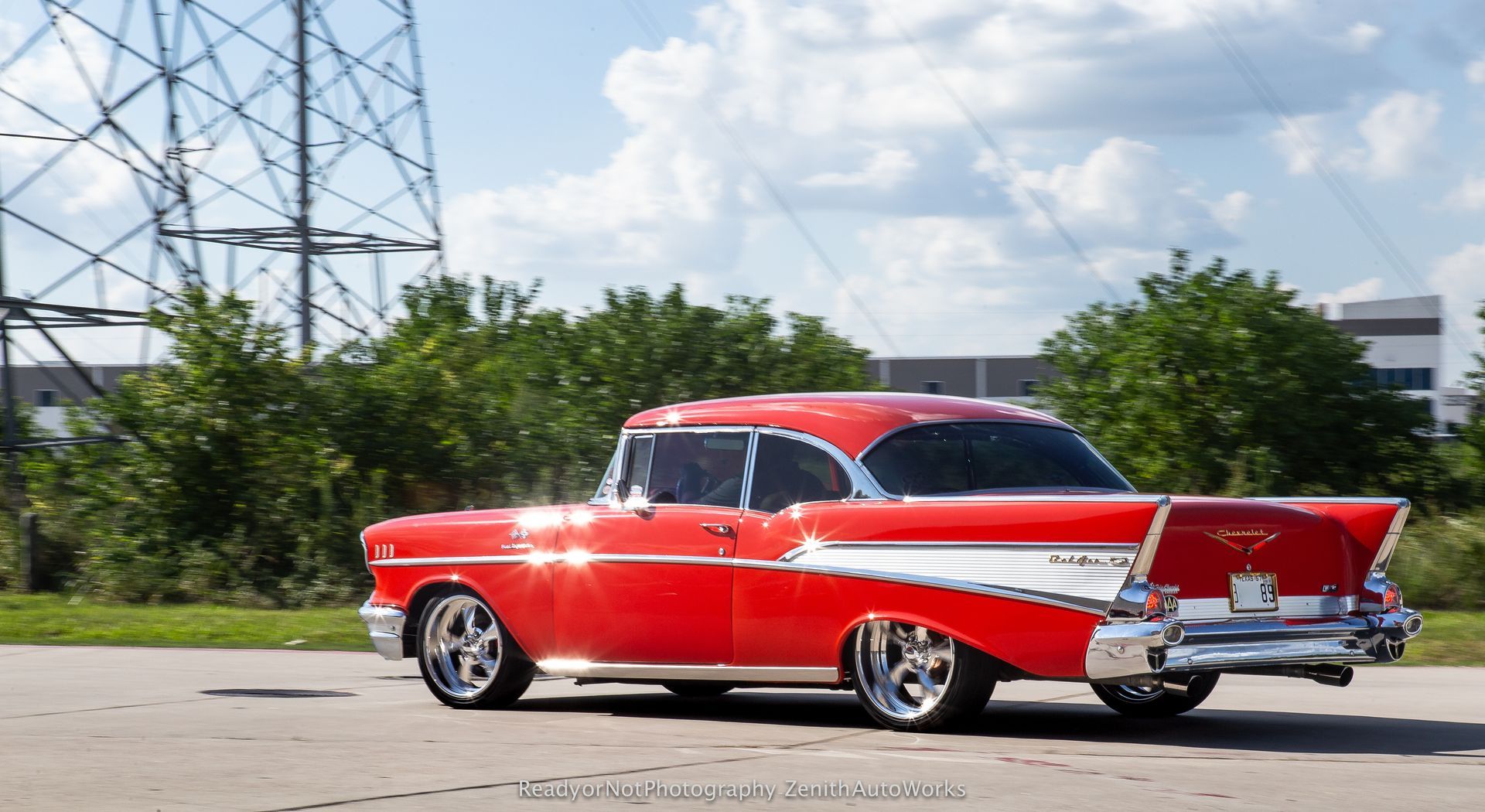 Red, customized 1957 Chevrolet Bel Air with chrome accents parked on asphalt.