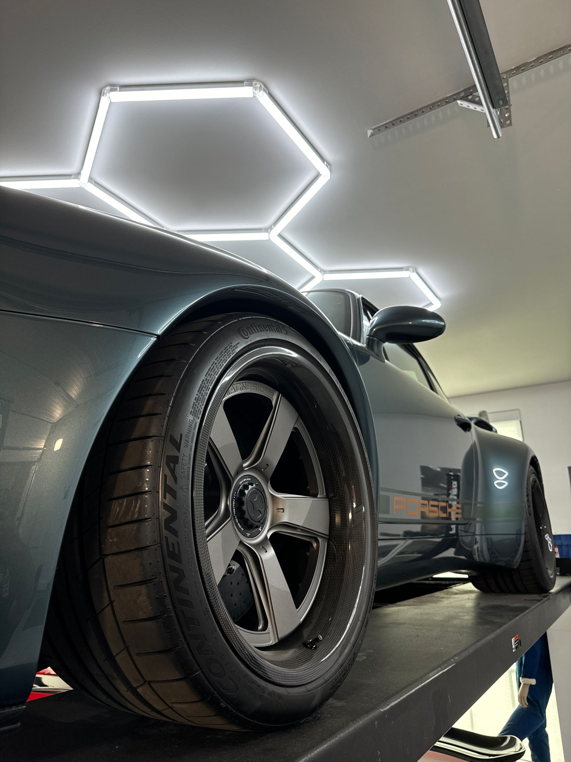 Dark teal sports car on a lift; hexagonal ceiling lights.
