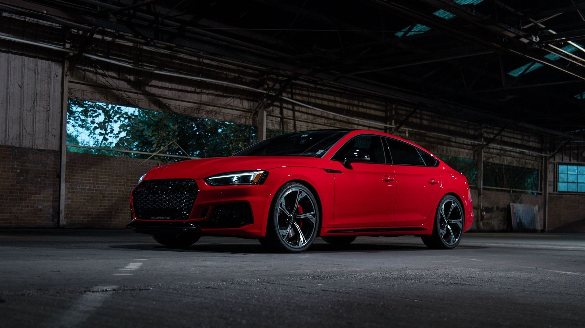 Red Audi sedan parked in a dimly lit industrial space; black wheels, dark accents.