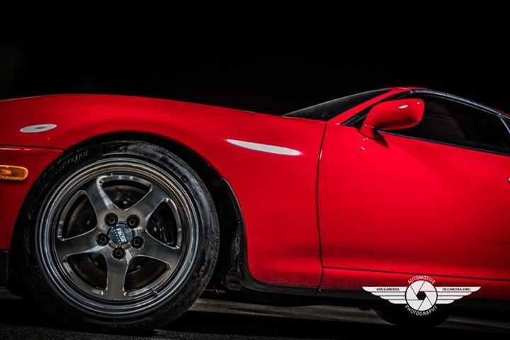 Red sports car, side view, dark rims, against a black background.