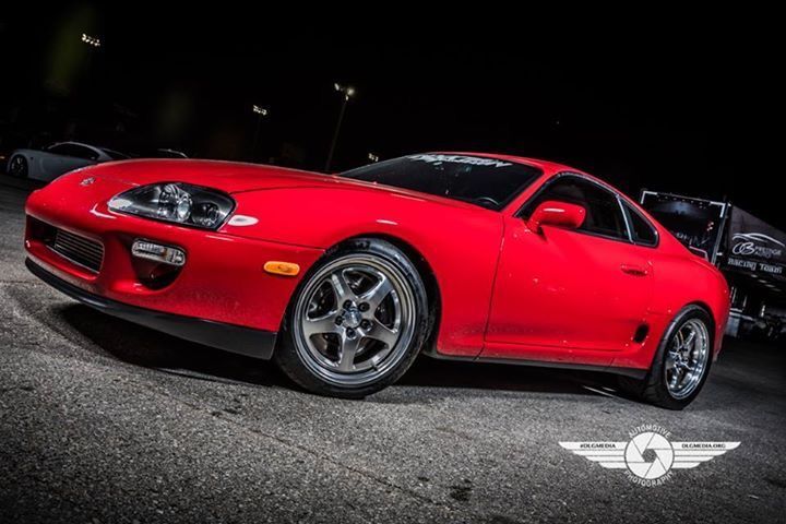 Red Toyota Supra sports car on an asphalt road at night, chrome wheels.