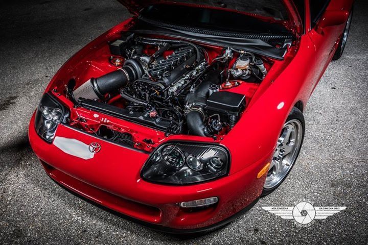 Red Toyota Supra with its hood up, revealing a black engine.